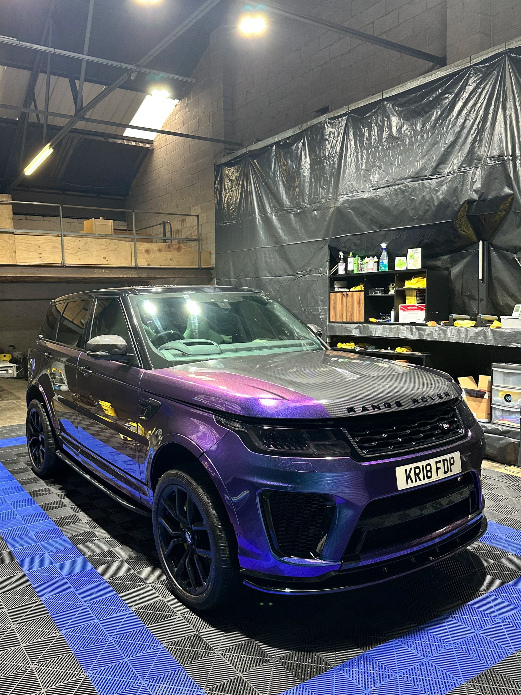Purple Range Rover parked inside a garage with black and blue checkered flooring and tools on a shelf in the background.