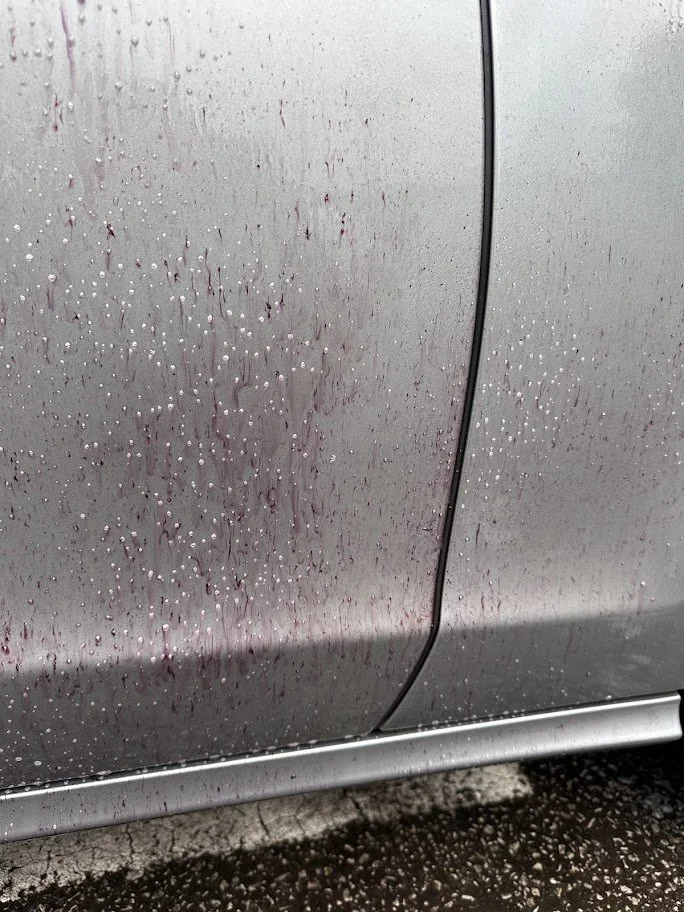 Close-up of a car door with raindrops and streaks of water on a gray, metallic surface.