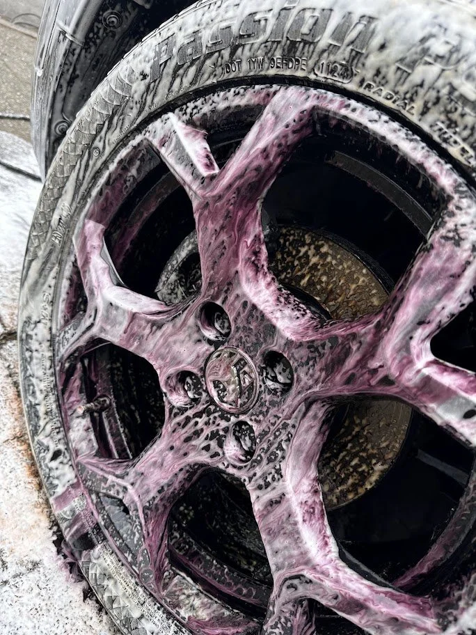 Car wheel being washed with pink foam soap and water.