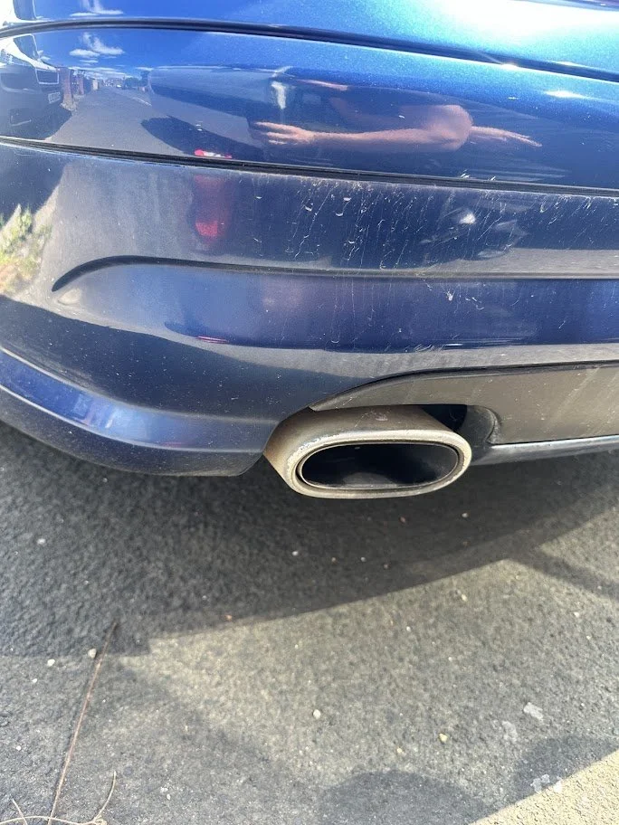 Close-up of the rear bumper of a blue car, showing some scratches and a single exhaust pipe.