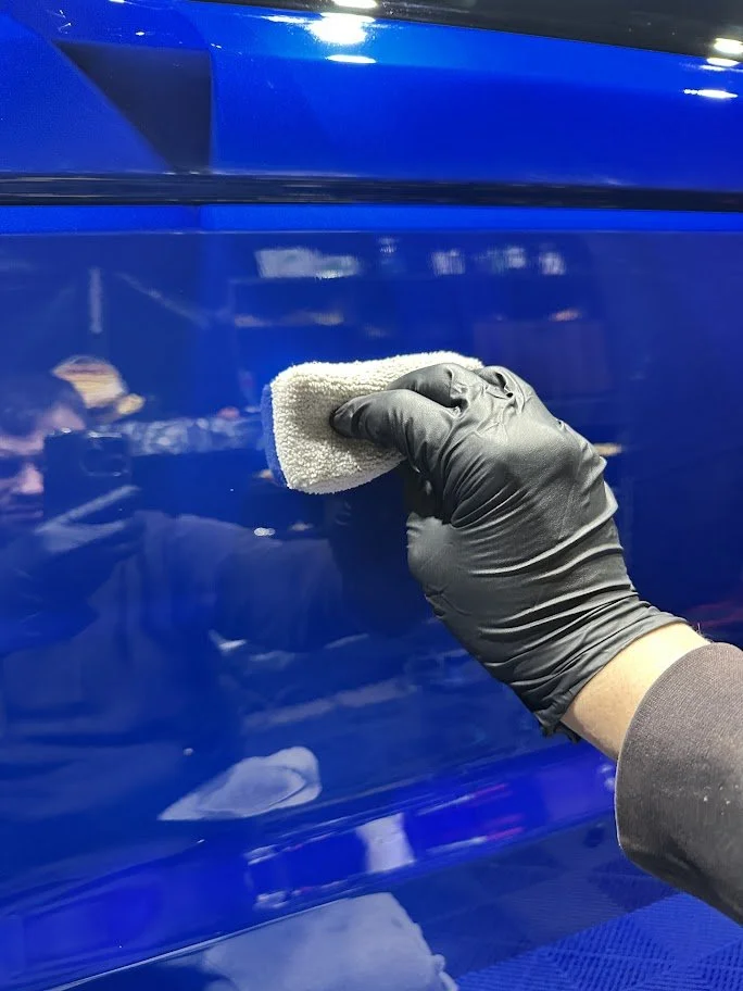 A person wearing a black glove is polishing a shiny blue surface with a white cloth.
