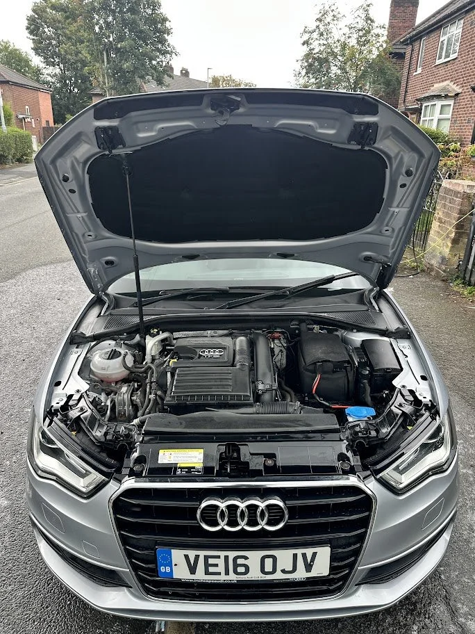 Front view of a silver Audi car with the hood open, showing the engine compartment.