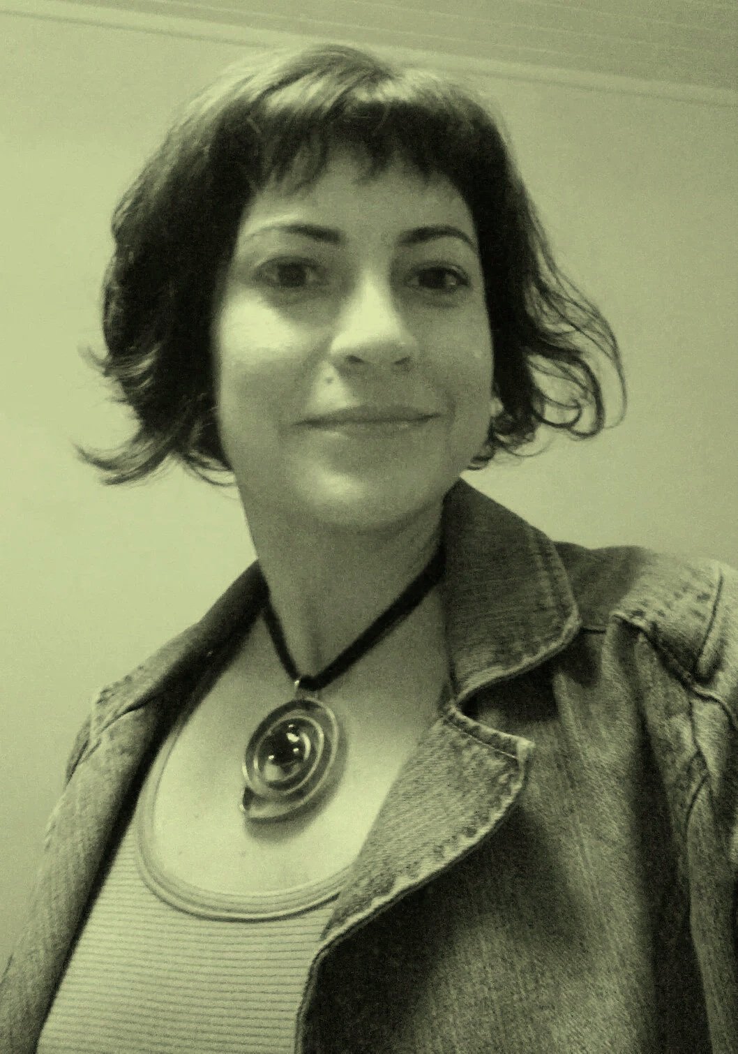 Retrato de uma mulher com cabelo curto e bagunçado, usando jaqueta jeans e colar de espiral, em tom sépia.