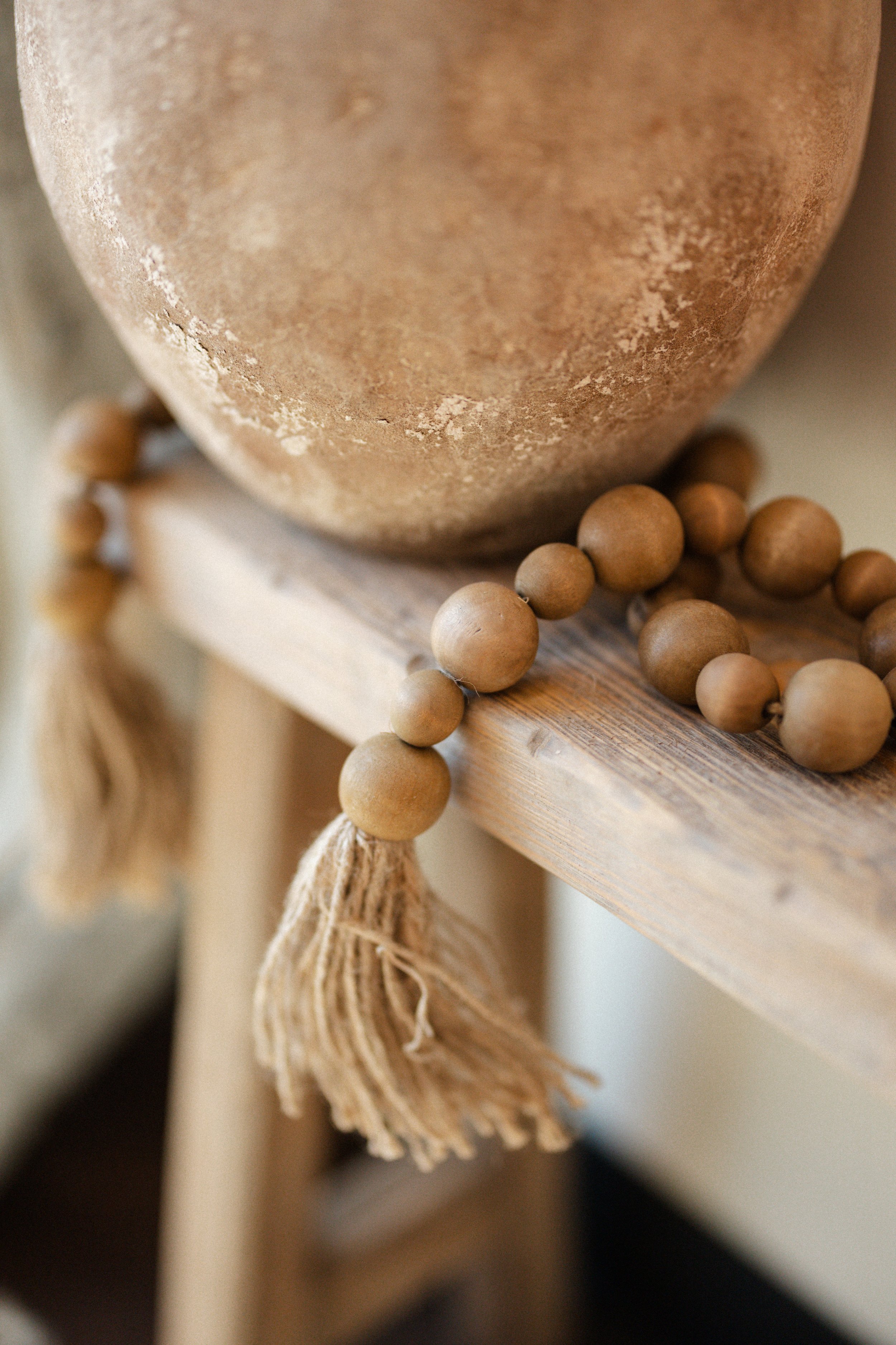 Close-up of a round, textured clay pot with a wooden bead garland draped over a wooden surface in a neutral, warm tone. Defy RS | Daxxify & Lip Filler in Pueblo West CO