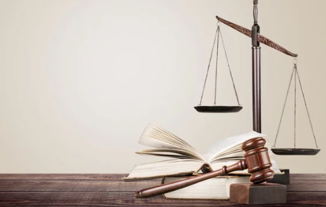 Scales of justice, open legal book, and gavel on wooden surface.
