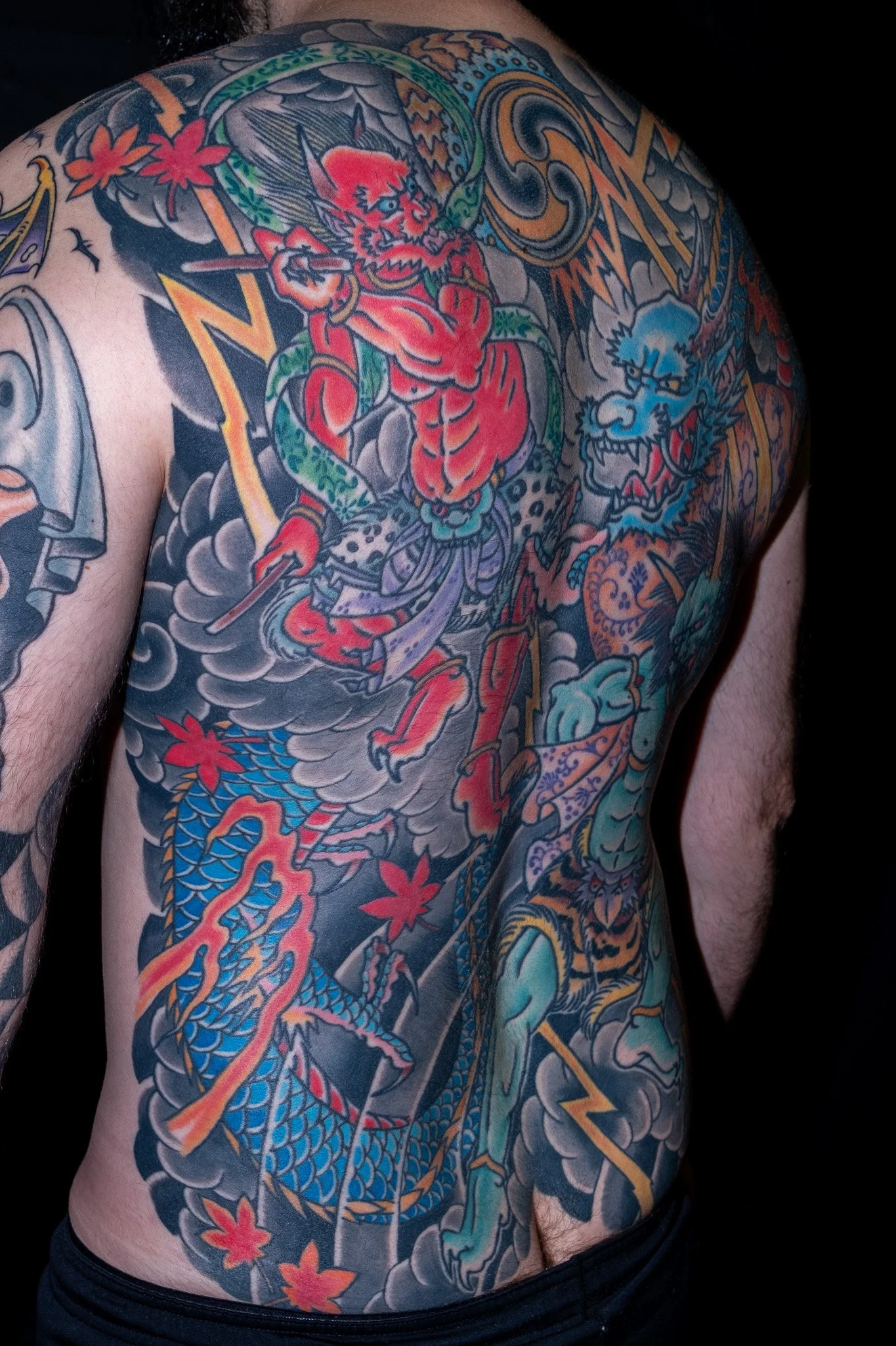 Colorful Japanese-style dragon tattoo covering a person's shoulder and chest, featuring a dragon with scales, clouds, and cherry blossoms.
