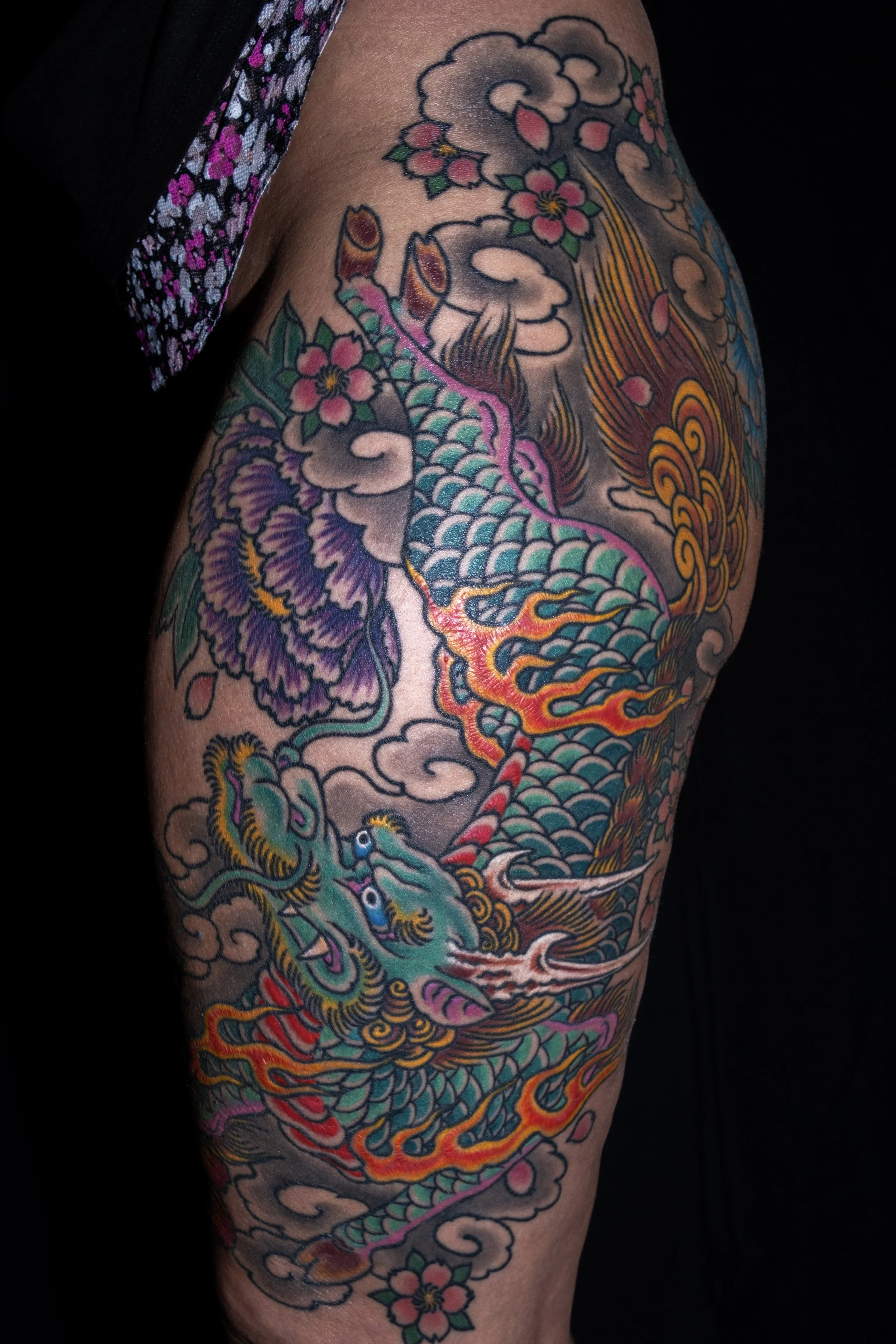 Colorful traditional Japanese tattoo depicting a dragon intertwined with cherry blossoms and clouds on a person's arm. Tattoo by Joe Haasch. 