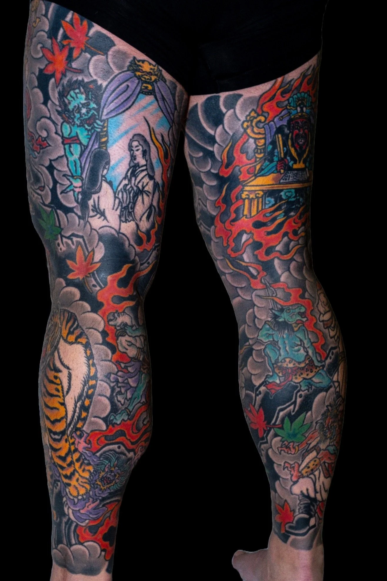 Tattooed legs with Japanese-style tattoo art, including flames, a dragon, a tiger, and a woman dressed in traditional clothing.