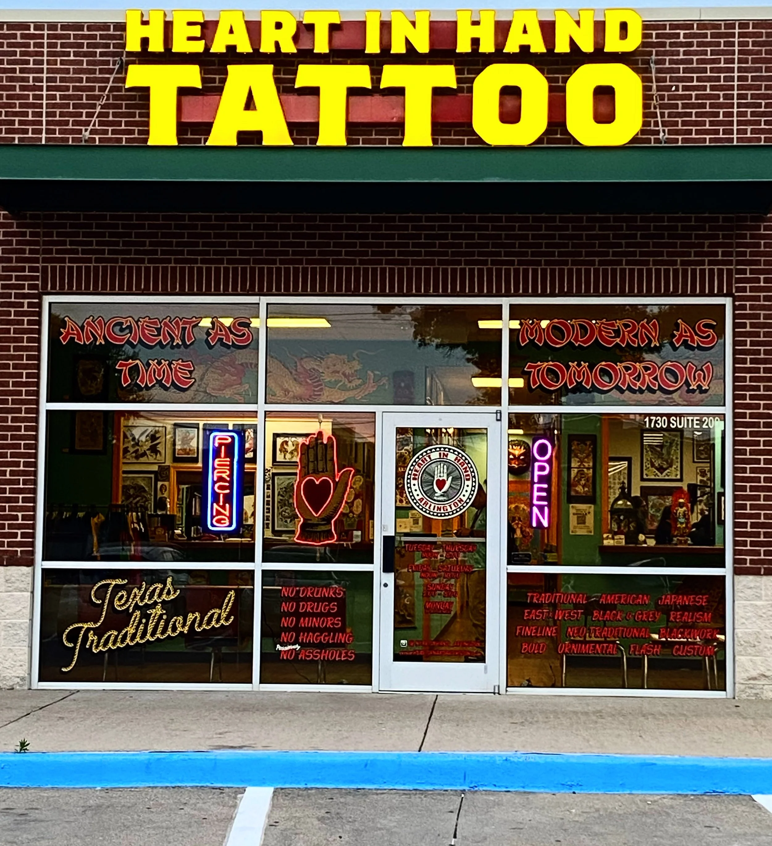 storefront with a large yellow sign that reads 'HEART IN HAND TATTOO' and Asian-themed decoration on the windows, with neon signs including 'OPEN' and 'NO DRUGS, NO MINORS, NO HATTLING, NO ASSHOLES' displayed in the window.