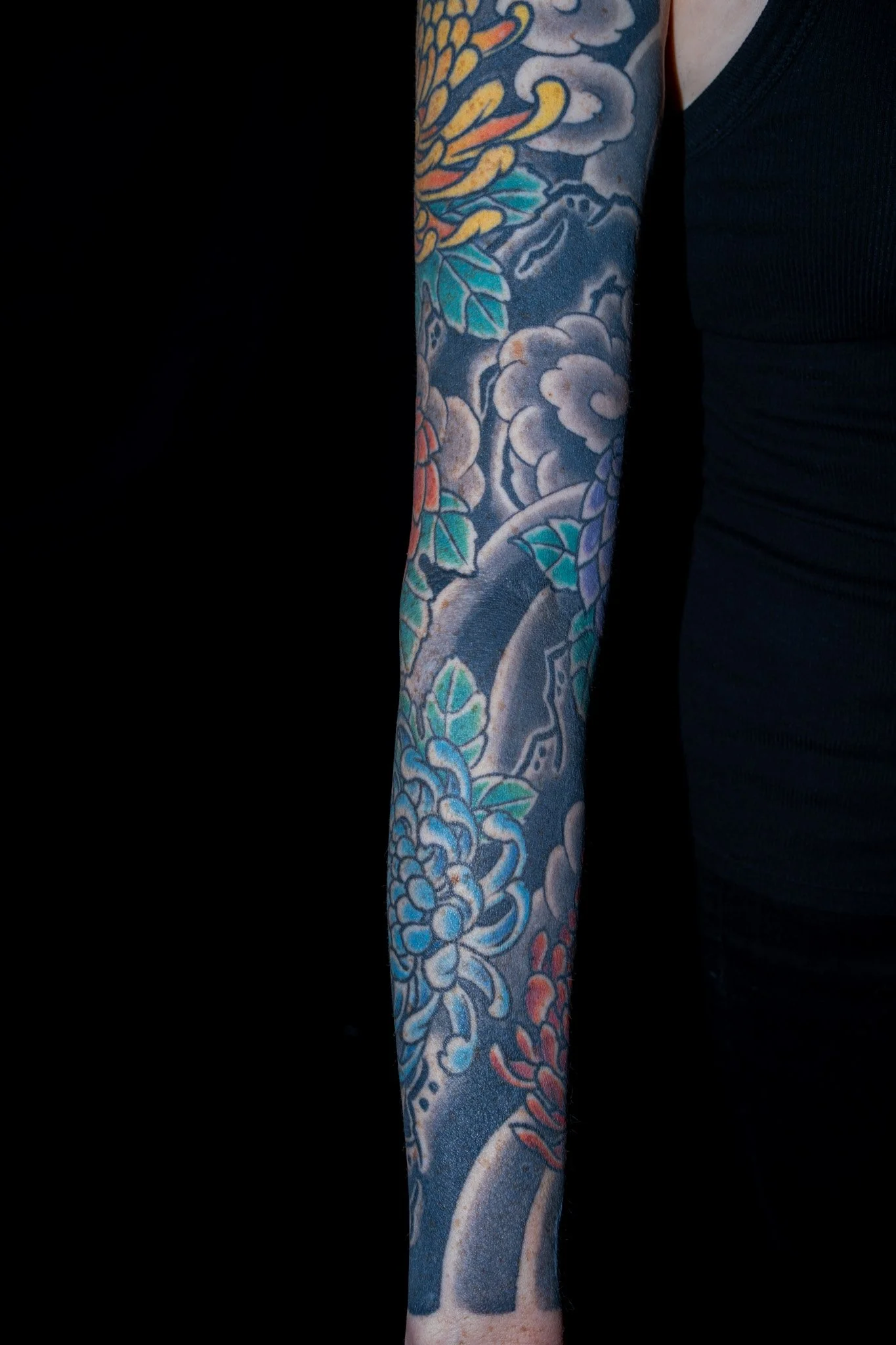 Close-up of a person's arm covered in a colorful traditional Japanese-style tattoo with flowers, clouds, and a snake design. Tattoo by Joe Haasch. 