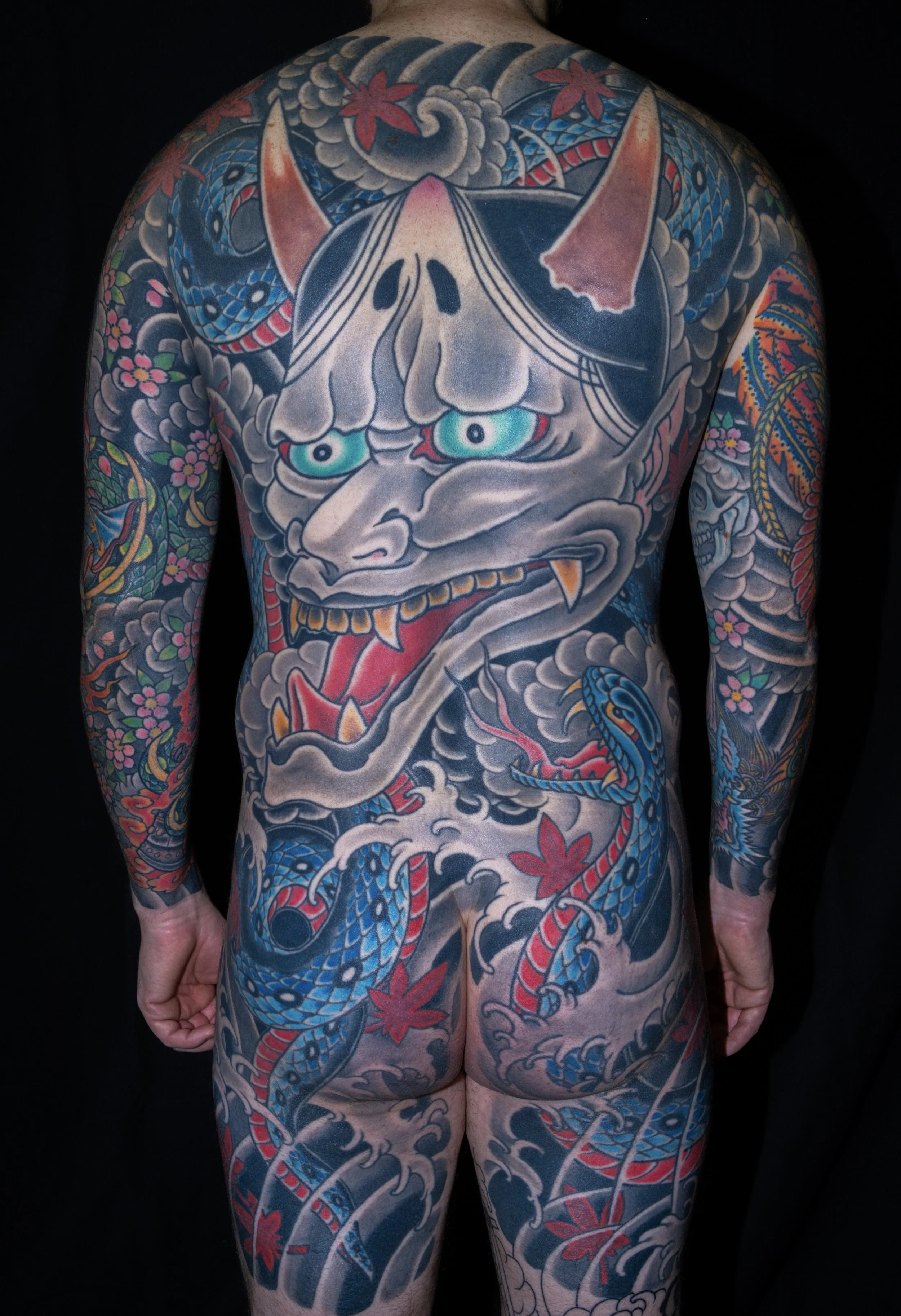 Full back tattoo of a traditional Japanese-style dragon with blue scales, red accents, and clouds.