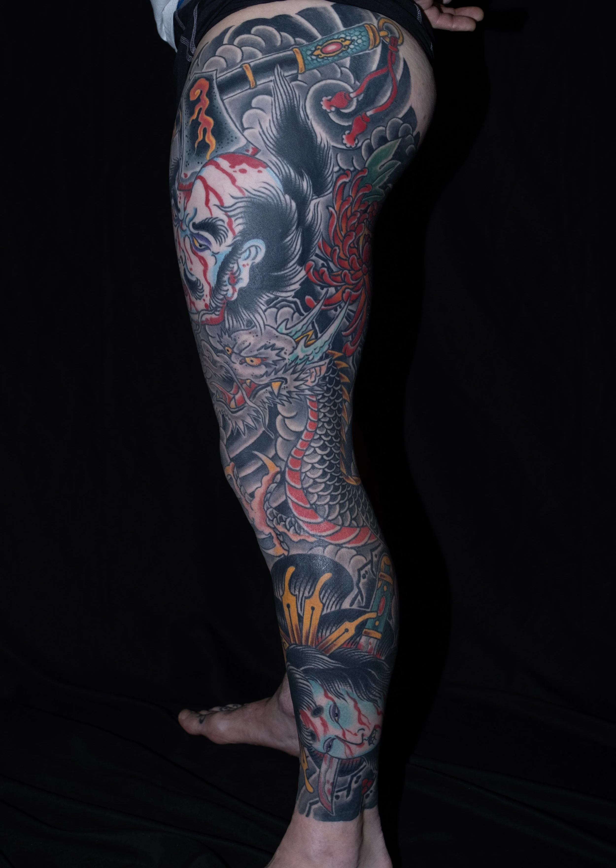 Tattooed arm featuring a detailed and colorful design of a fierce Asian dragon intertwined with clouds, waves, and floral elements. Tattoo by Joe Haasch. 