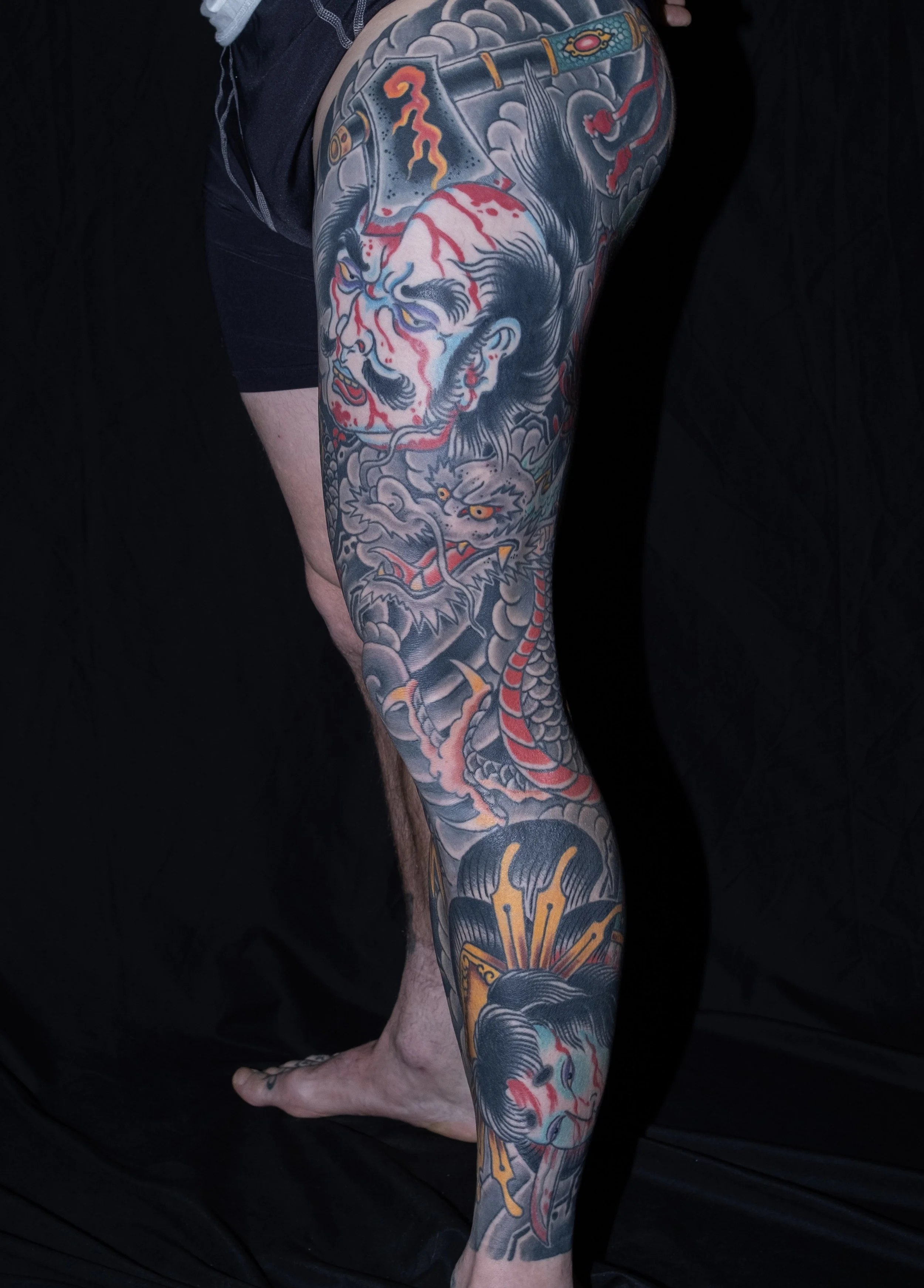 Full-color tattoo sleeve featuring a fierce oni mask, a traditional Japanese tiger, clouds, and other elements, covering the person's upper arm and shoulder.