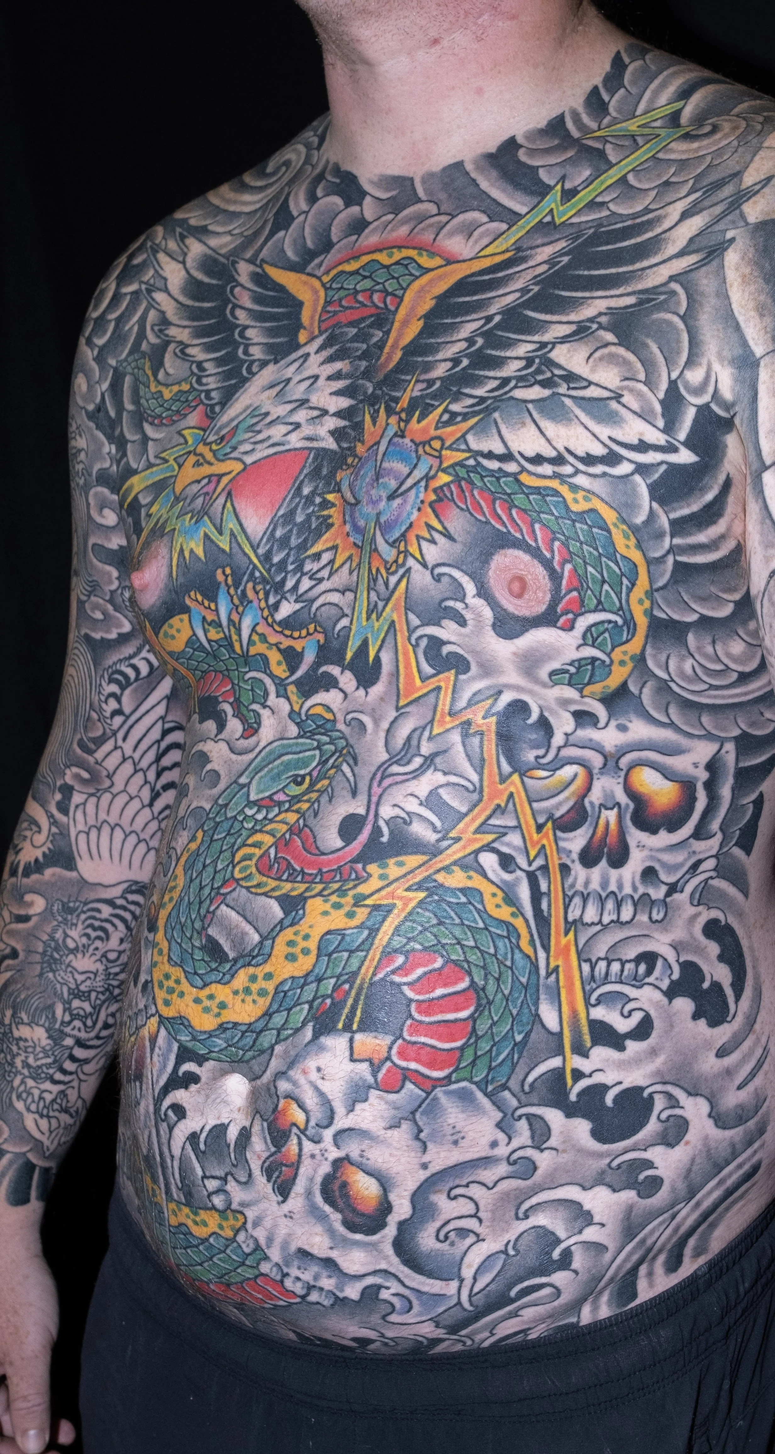Colorful tattoo of a snake, eagle, skulls, clouds, and lightning on a man's chest and shoulder.