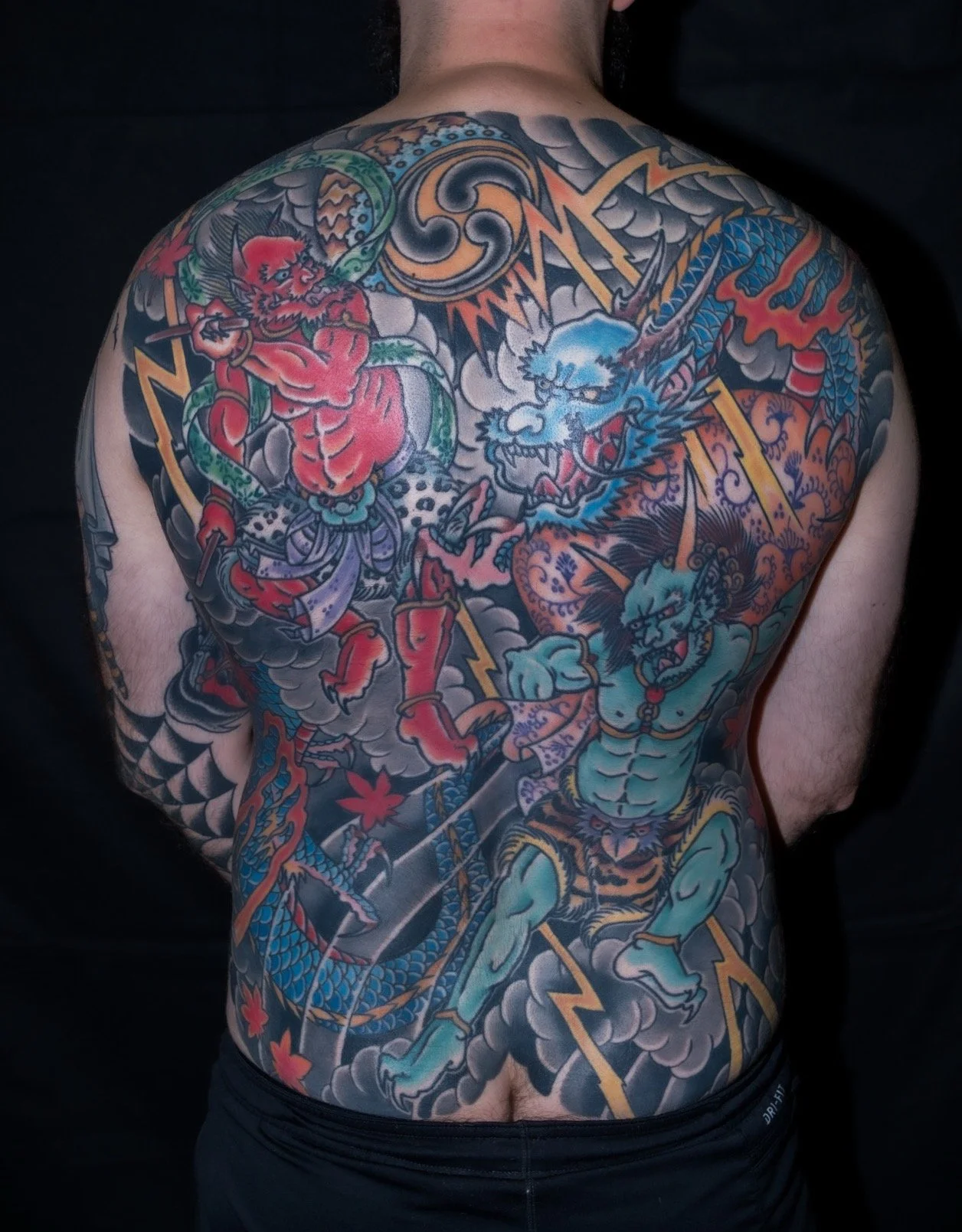 Colorful Japanese-style tattoo covering the person's back, featuring a dragon and a mythical creature, with clouds and lightning elements.