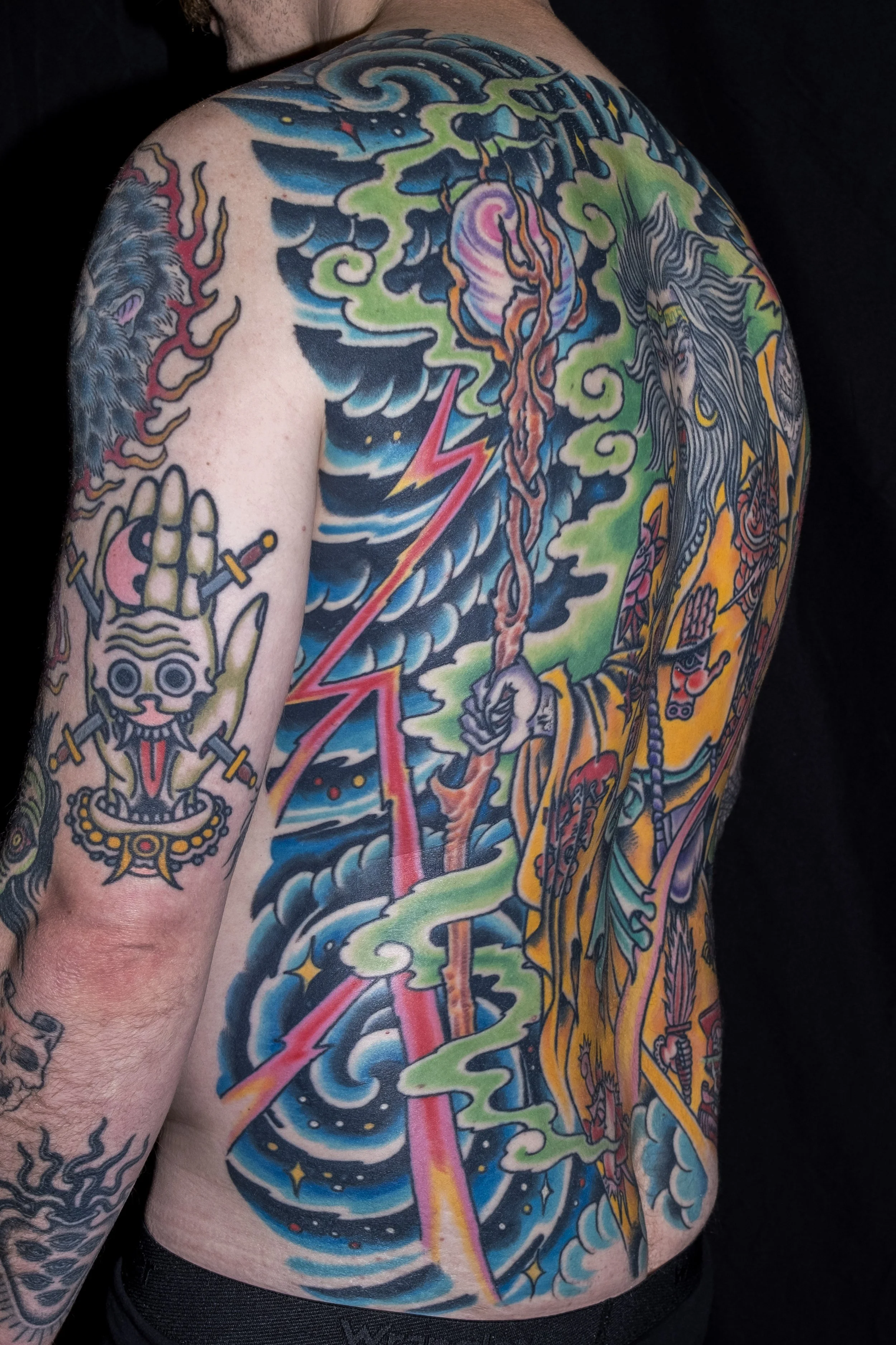 Colorful tattoo sleeve featuring a skull, lightning bolt, a female figure with flowing hair, and cosmic elements on a person's arm and side torso.
