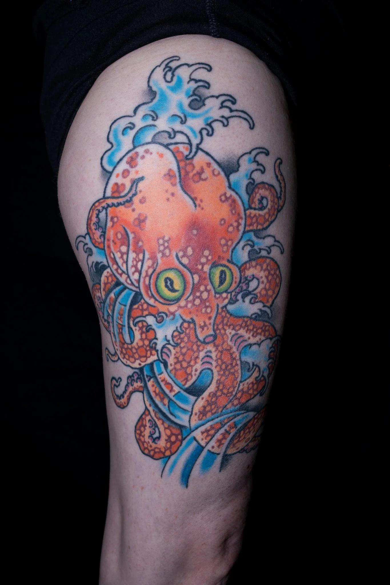Tattoo of an orange octopus with blue water splashes on a person's upper arm. Tattoo by Joe Haasch. 