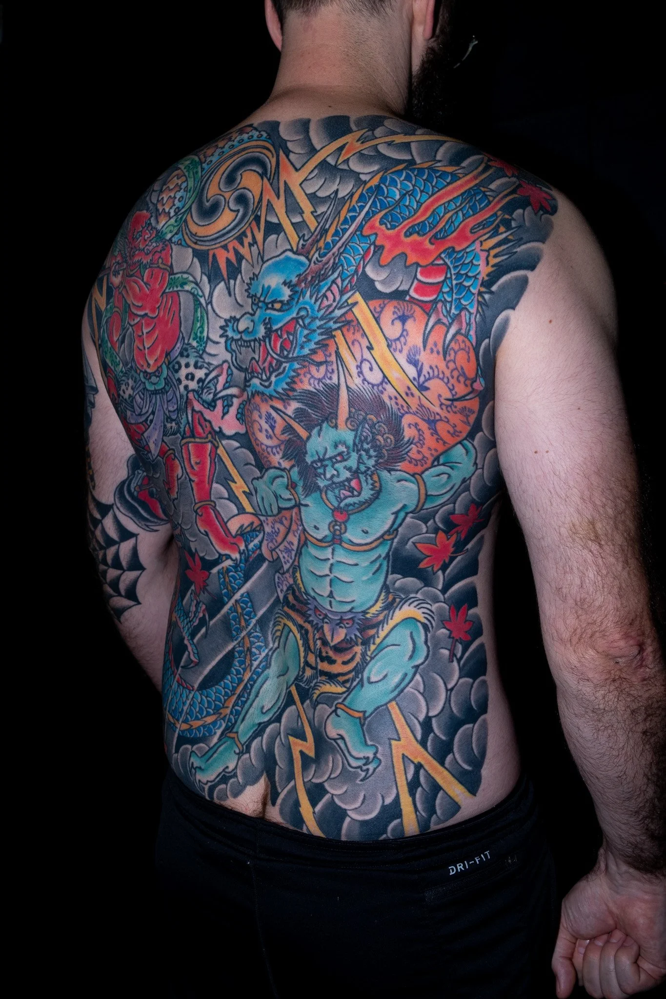 Colorful traditional Japanese-style tattoo covering the upper body and arm of a man, featuring a dragon, clouds, lightning bolts, and a fierce lion.