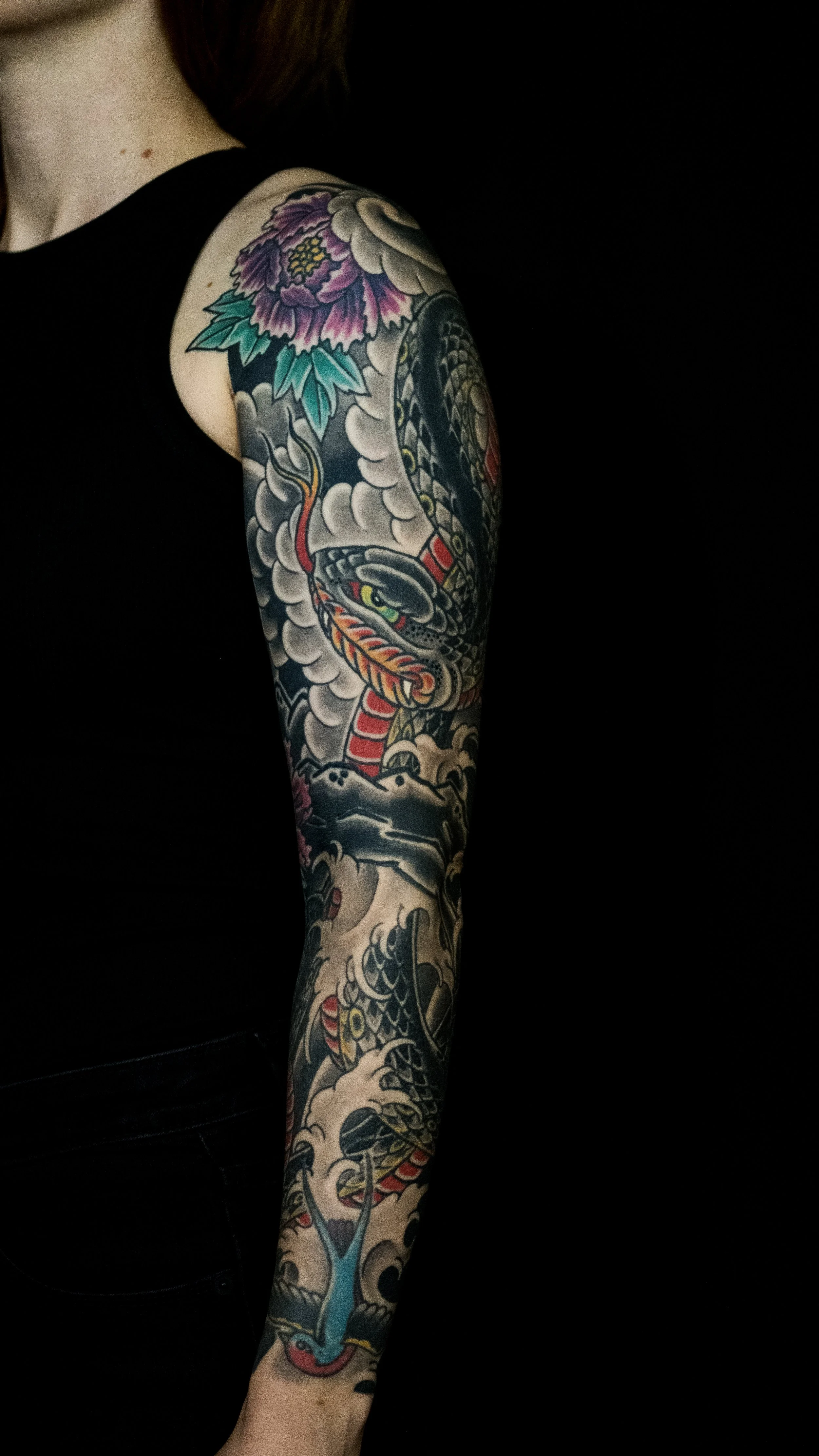 A person's arm covered in a colorful Japanese-style tattoo of a dragon coiled around with clouds and a peony flower at the top. Tattoo by Joe Haasch. 