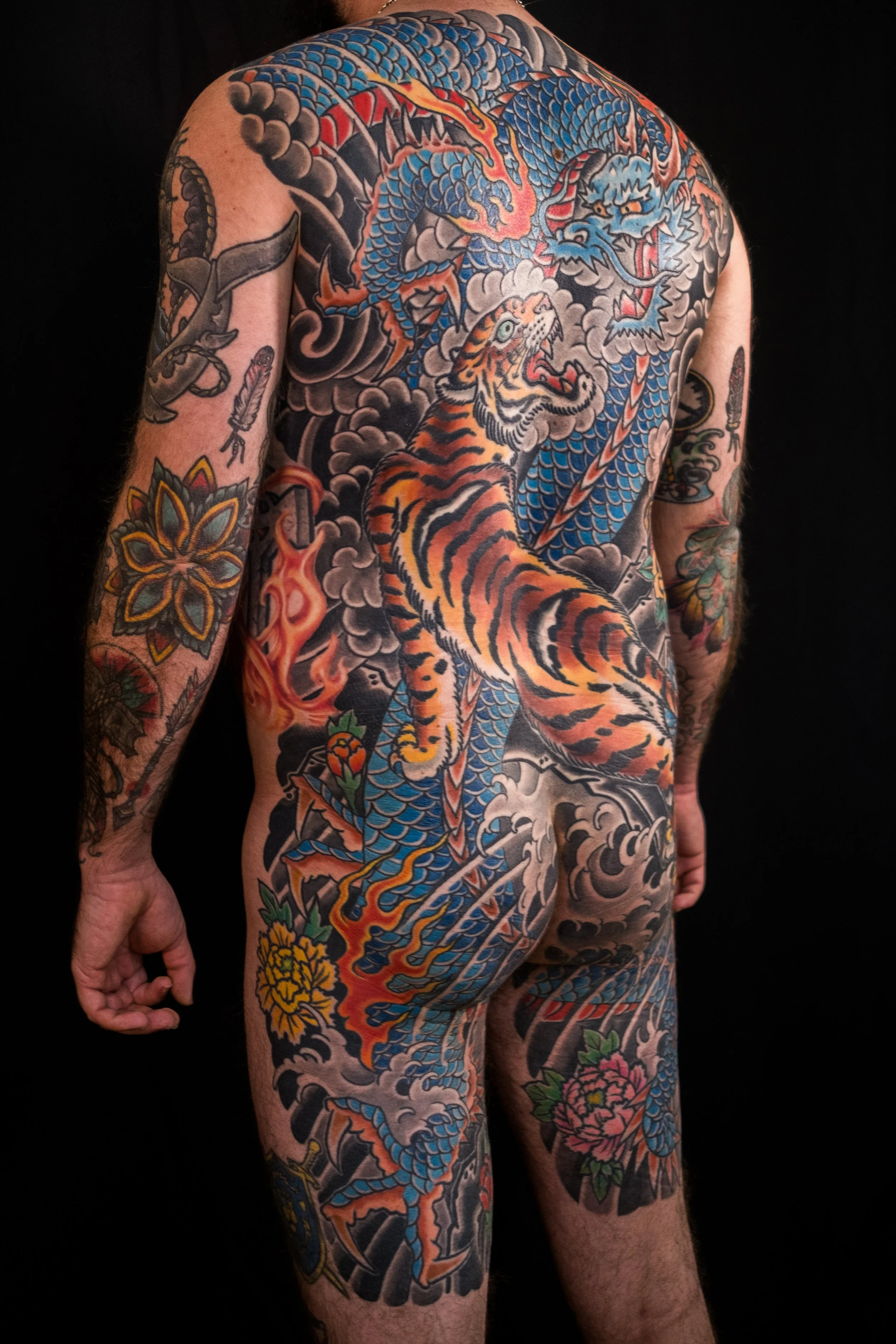 Full sleeve and torso tattoo of a traditional Japanese style dragon and tiger design with clouds and flames, covering the person's back, shoulder, arm, and side.