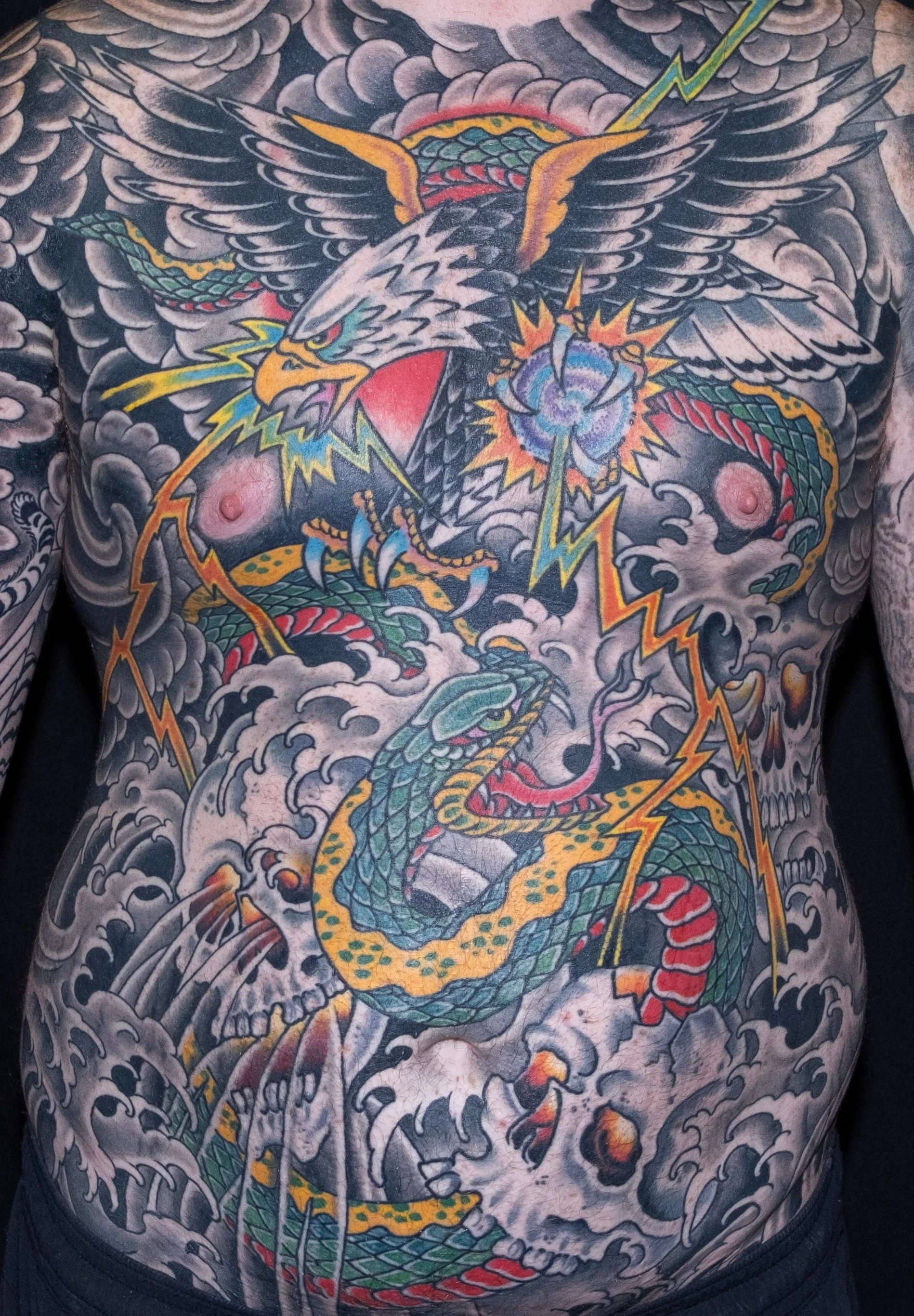 Colorful tattoo of an eagle with a snake in its talons, surrounded by stormy clouds and lightning.