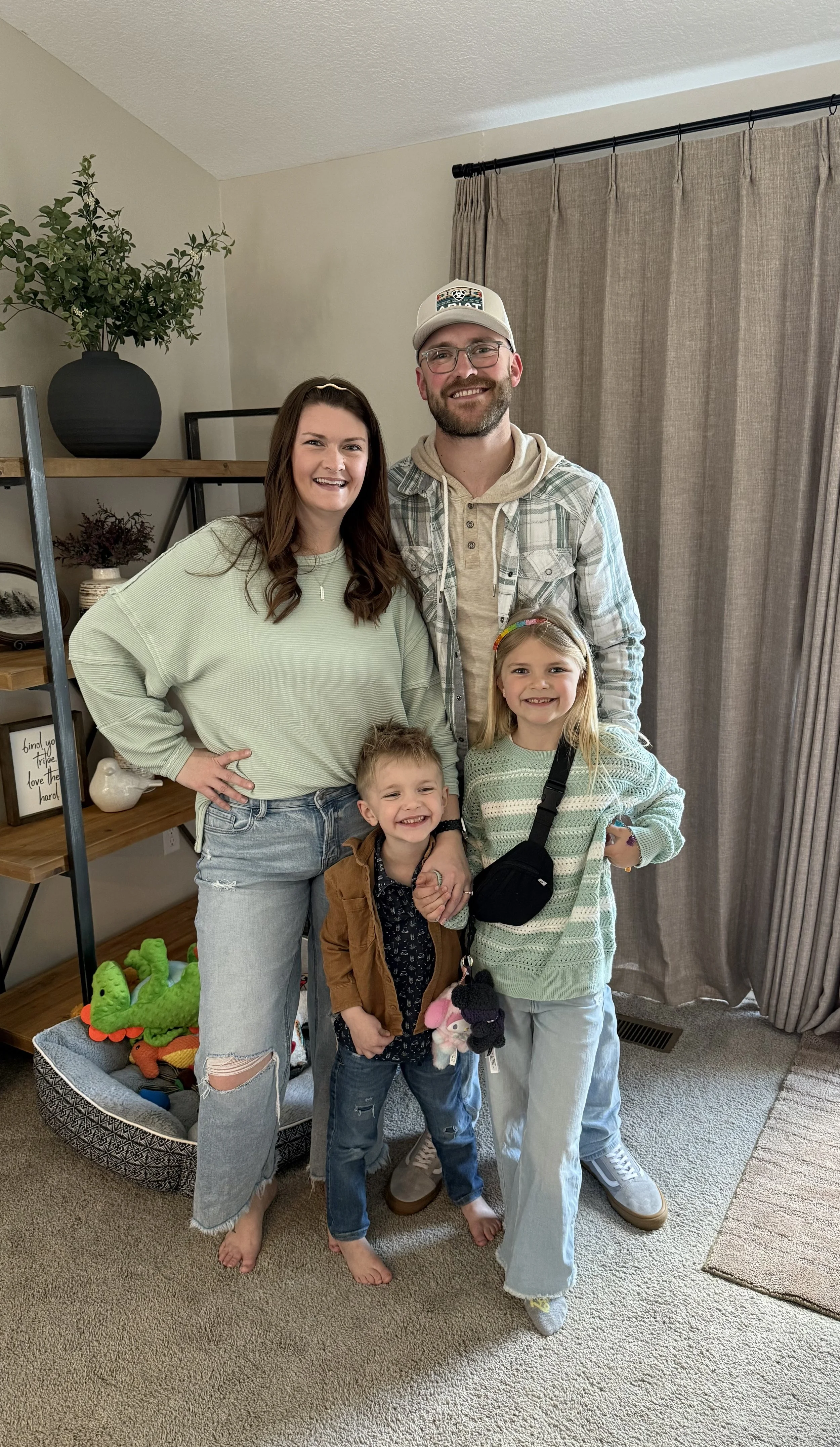 A family of five standing indoors, smiling at the camera. The family includes a woman, a man, and three children.