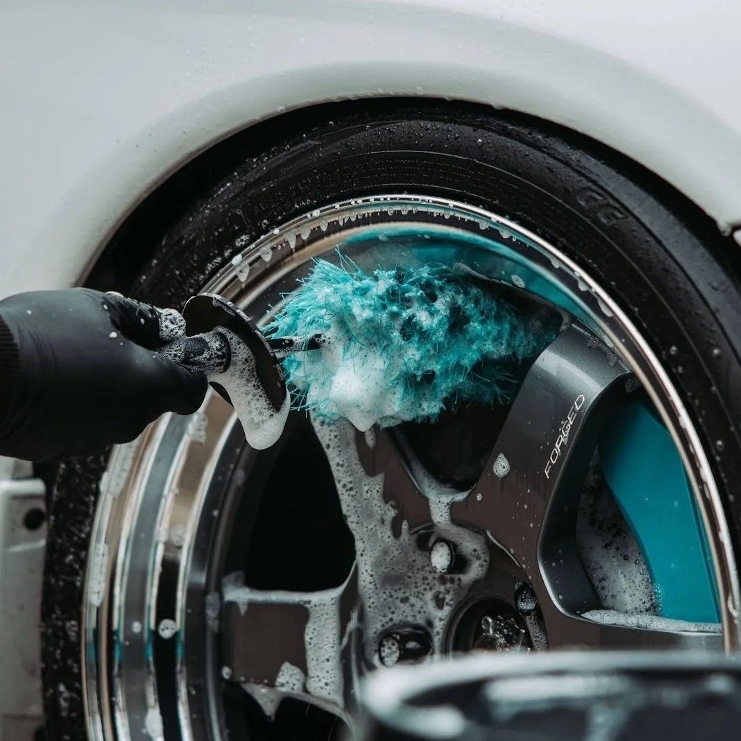Person cleaning a car wheel with a blue brush and soap.
