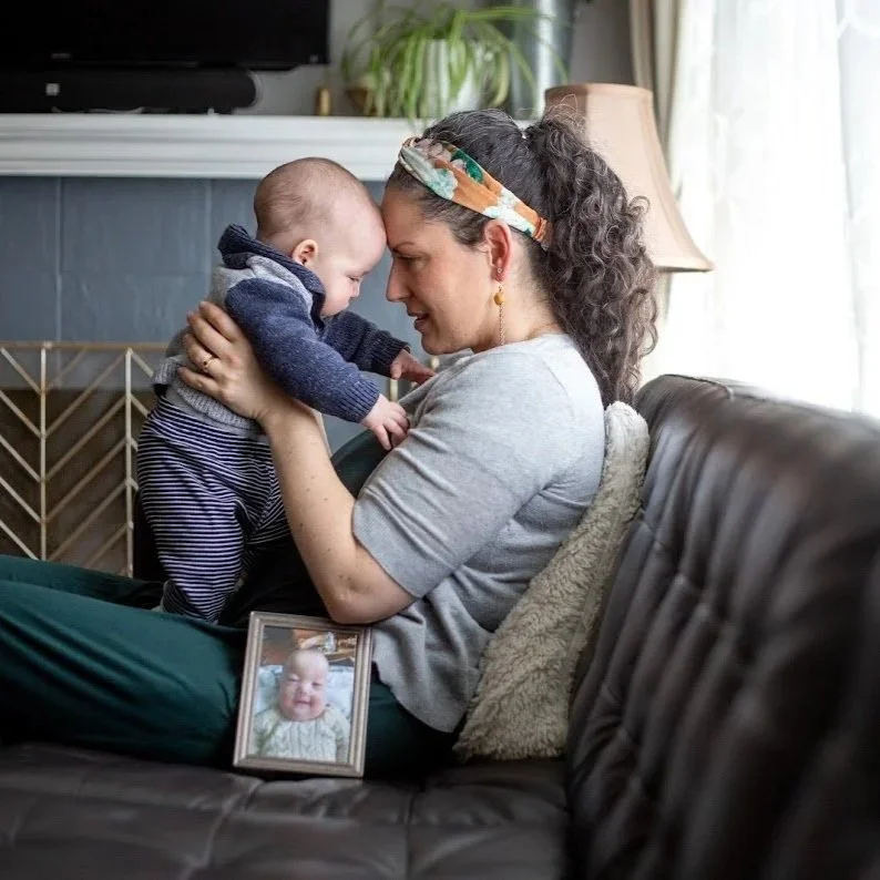 A woman and a baby are touching foreheads and sharing a joyful moment in a cozy living room, with a family photo on the sofa.