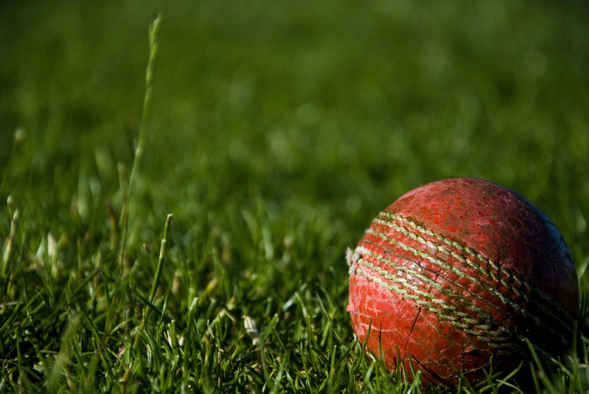 Close-up of a worn red baseball with white stitching lying on green grass.