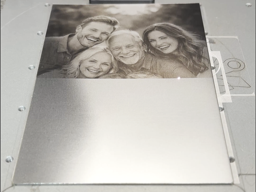 Ein graviertes Foto eines lachenden fünfköpfigen Familienporträts in Schwarz-Weiß, das auf eine Metallplatte graviert wird.
