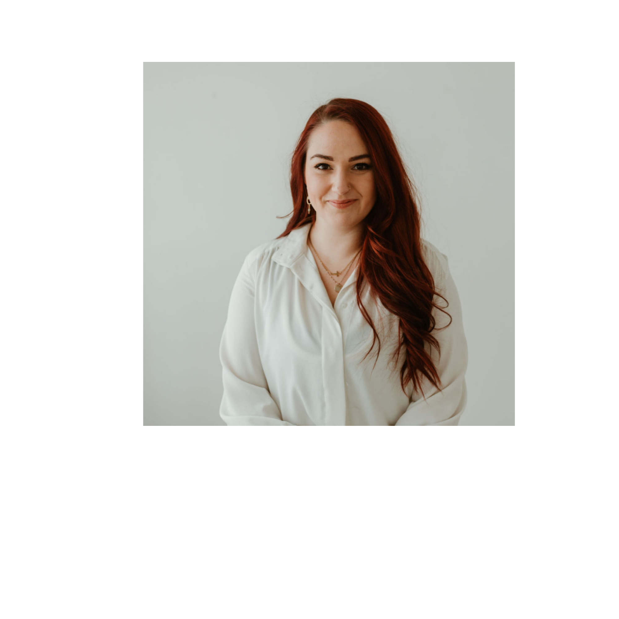 Rylee June owner of TCCS- with long red hair smiling, wearing a white blouse and layered necklaces, posed against a neutral background.