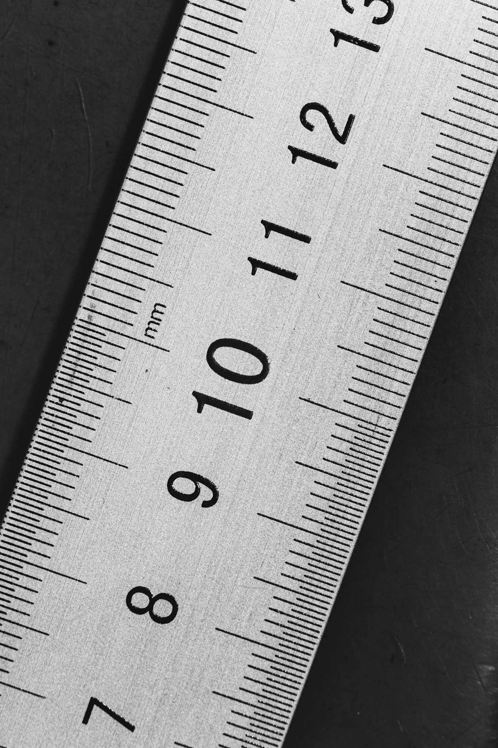 Close-up of a white ruler with black markings and numbers, placed on a dark surface.