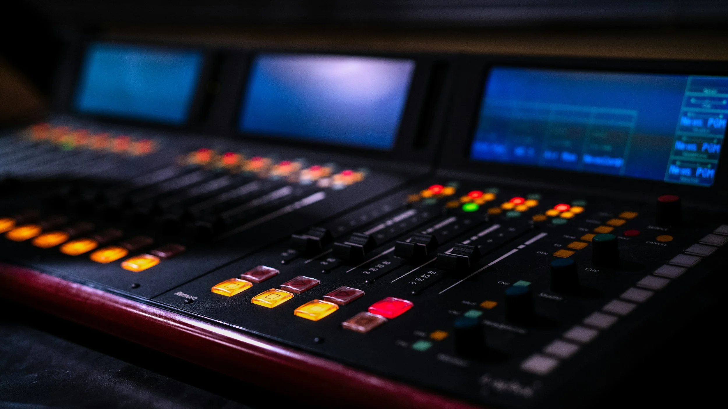 Close-up of a professional audio mixing console with illuminated buttons and digital screens.