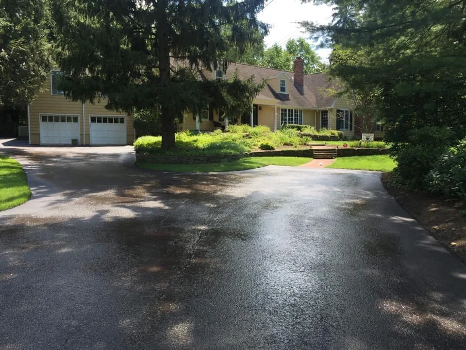 A yellow house with a driveway, surrounded by trees and a well-maintained lawn.
