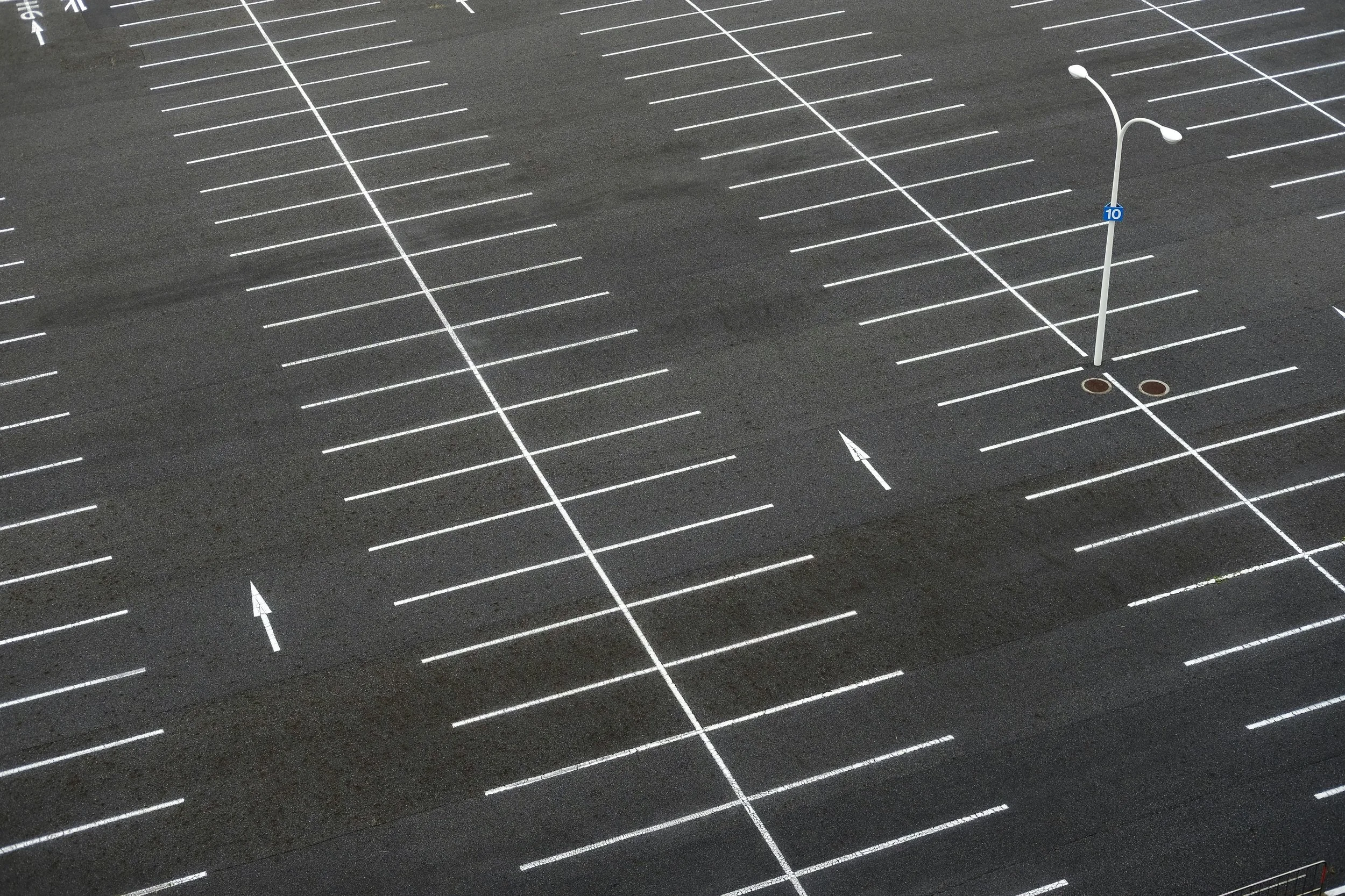 Empty parking lot with white painted parking spaces, two light poles, and directional arrows on the ground.