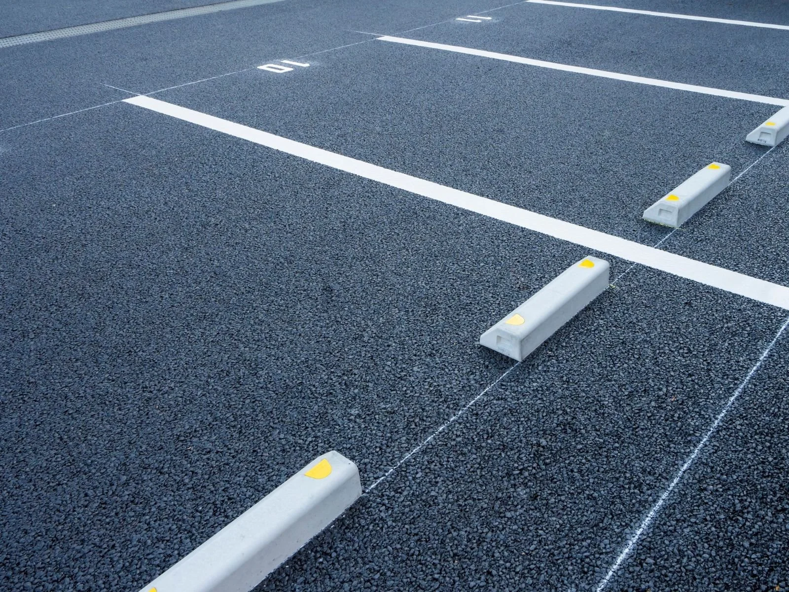 Empty parking lot with numbered parking spaces and white wheel stops on asphalt surface.
