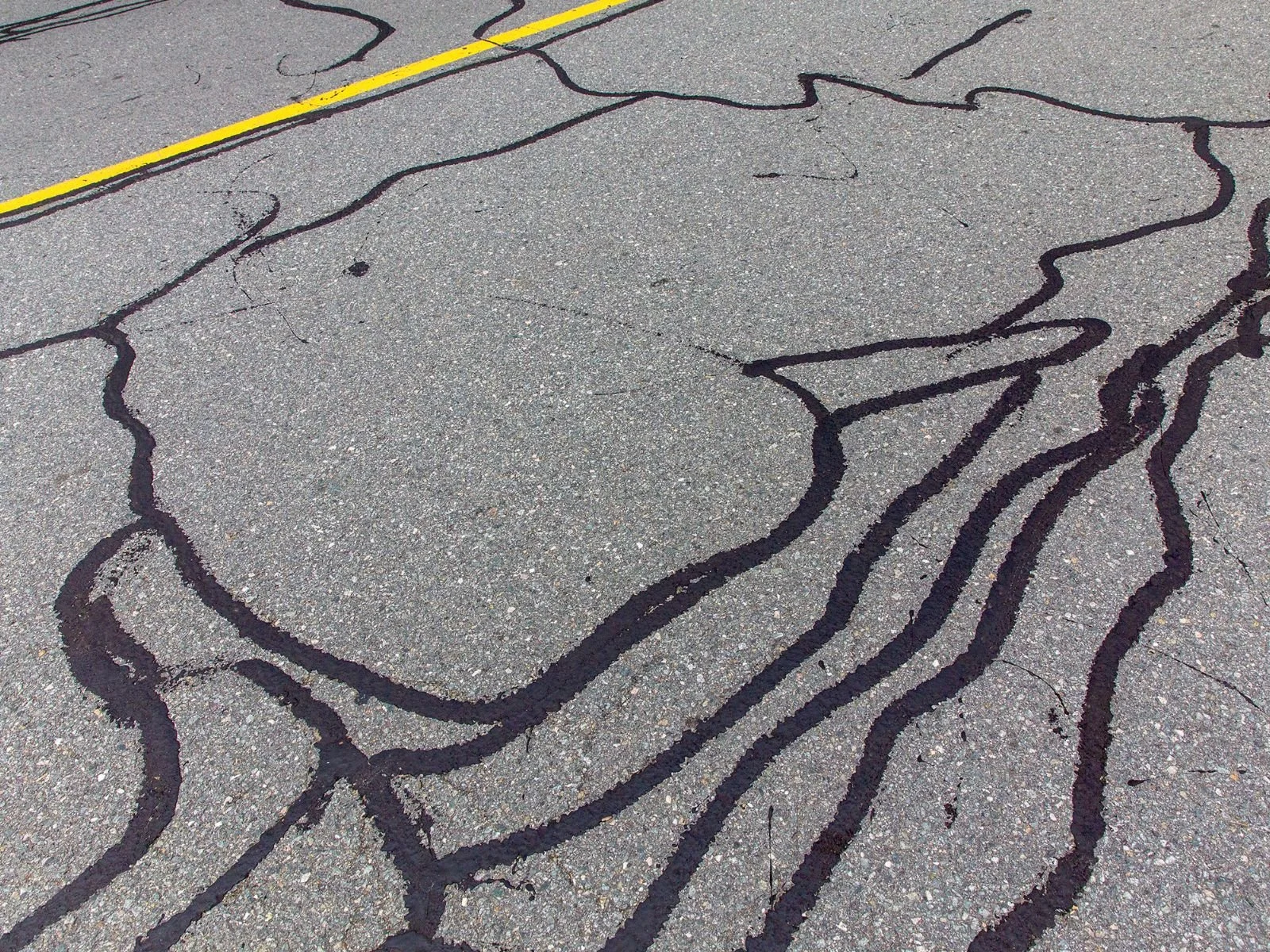 Cracked asphalt pavement with black oil or paint lines and a yellow line painted across the top.
