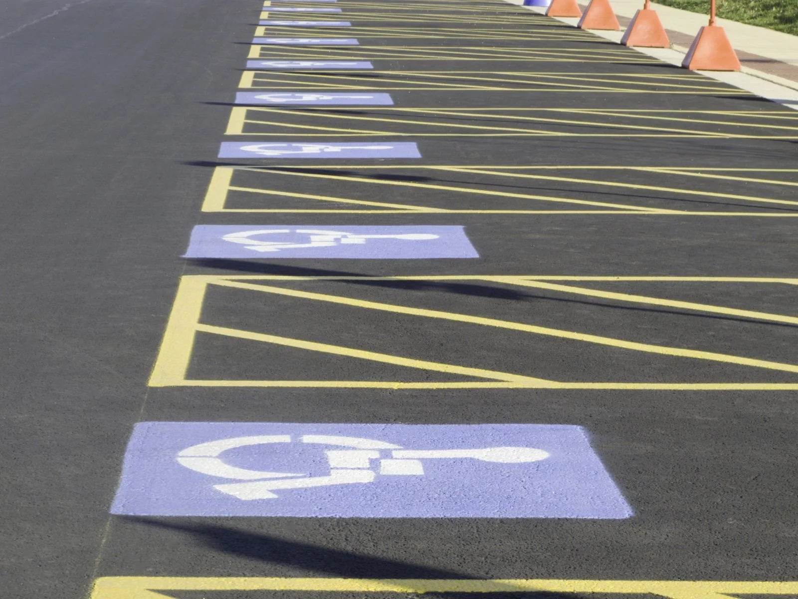 Empty parking lot with spaces marked for handicapped parking with blue painted signs and yellow lines, and orange cones along the sidewalk.