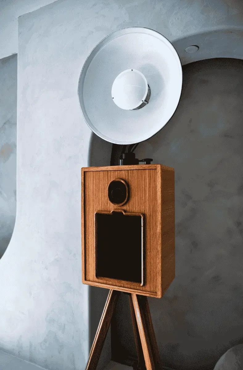 A vintage wooden speaker with a black screen and camera, on a tripod, with a large white dish-shaped object mounted above it
