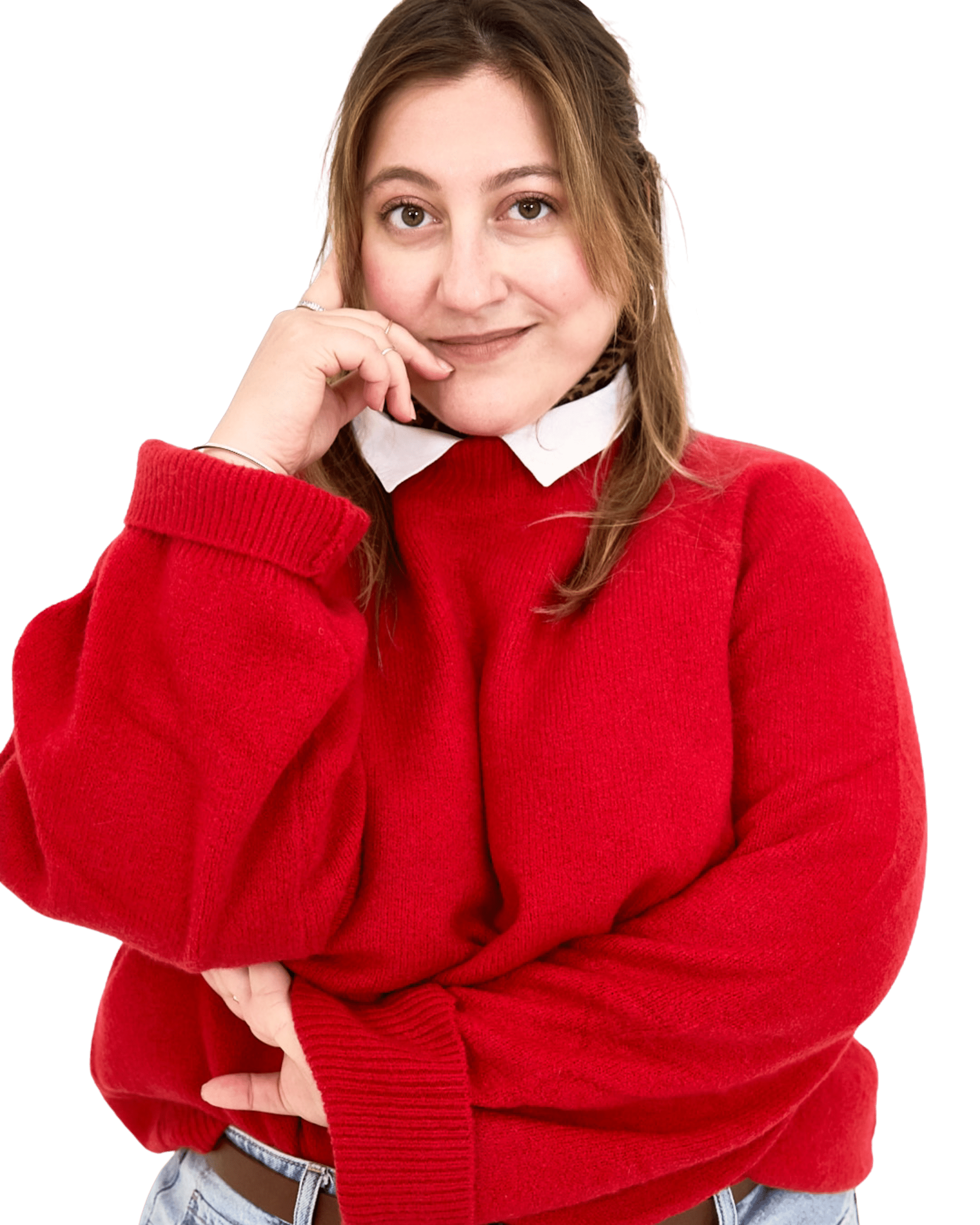 A woman with brown hair wearing a red sweater with a white collar and light blue jeans, smiling with her hand at her face, against a black background.