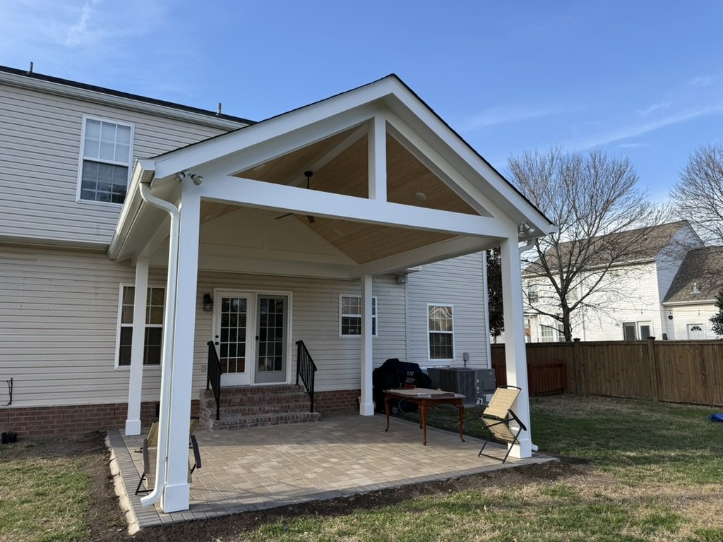 Backyard with a covered patio, brick steps, and a black grill on the patio with some outdoor furniture.
