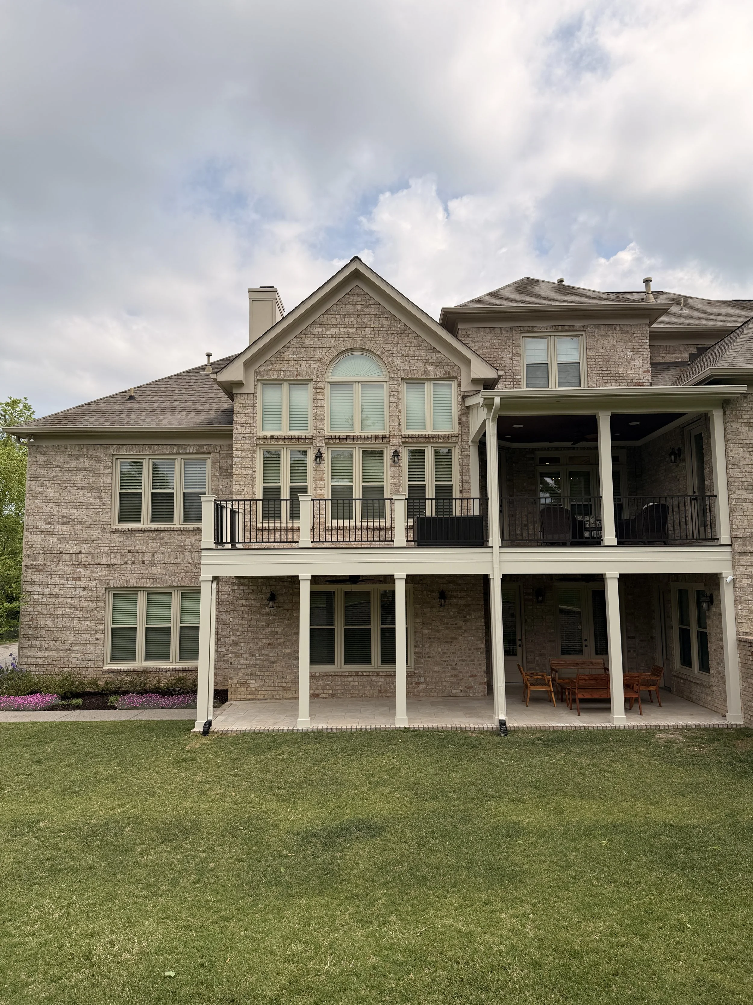Two-story brick house with large windows, a porch, and a backyard with a lawn and some flowers.
