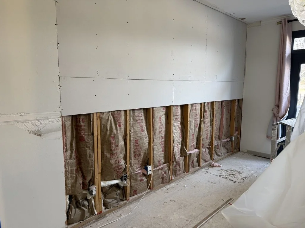Partially finished wall with drywall installed on upper section and insulation along the lower section; construction tools and materials visible in a room with a window.