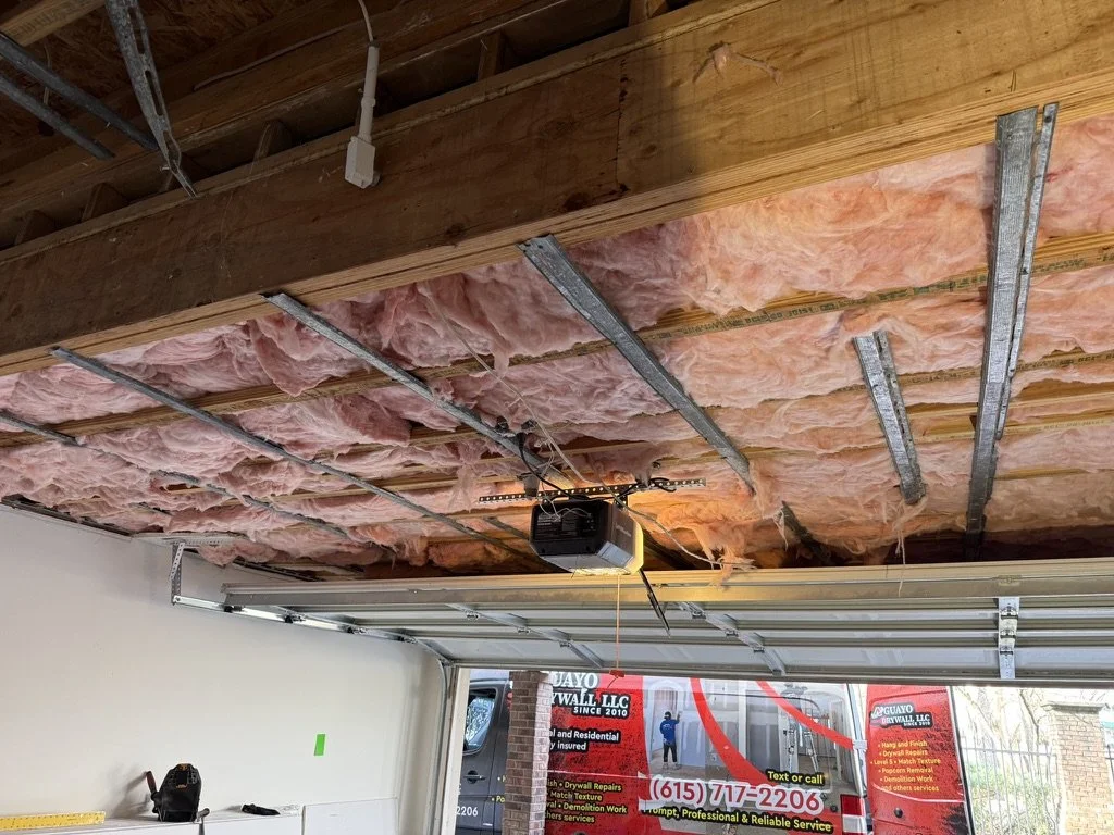 Garage ceiling with insulation and metal framing, garage door opener, emergency cord, and a work van outside with signage.