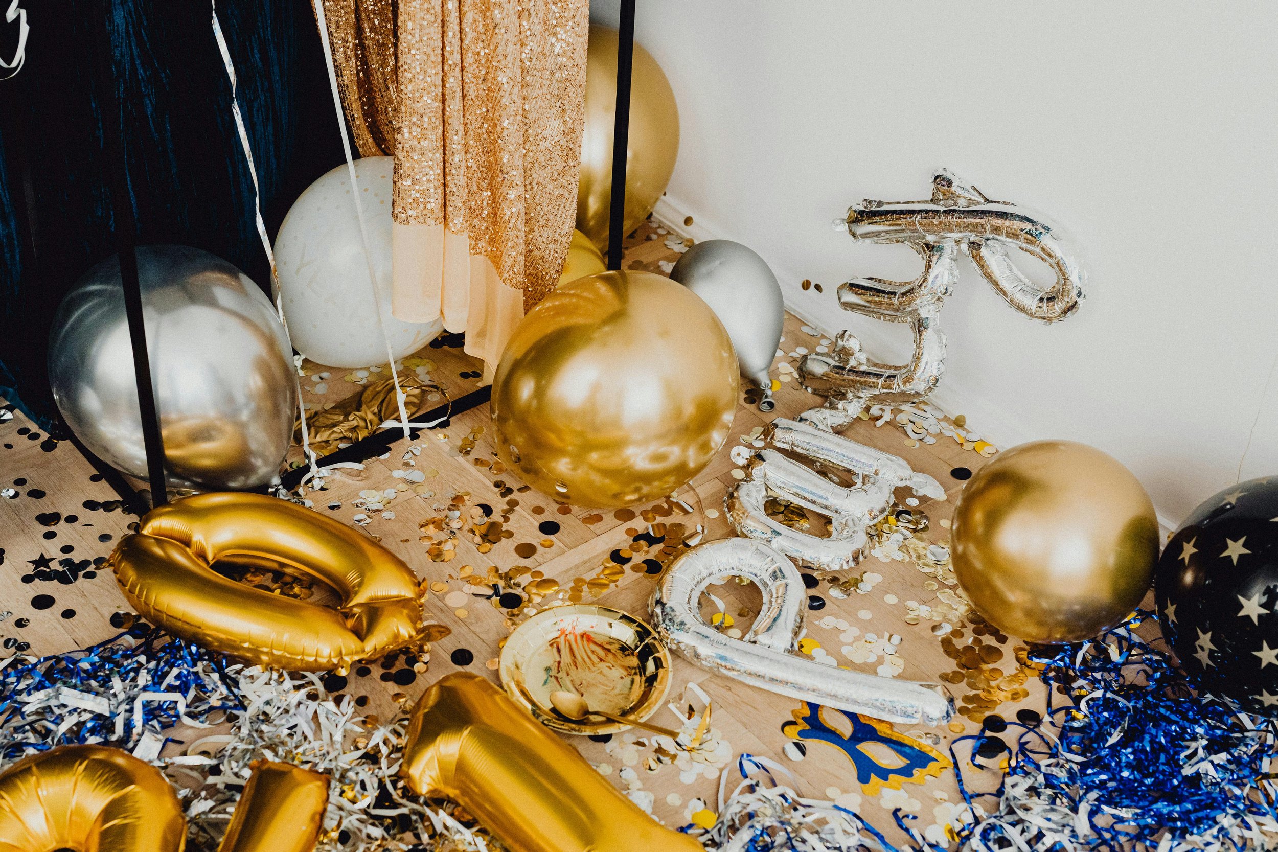 Party decorations including gold, silver, and black balloons, confetti, and party hats scattered on the floor.