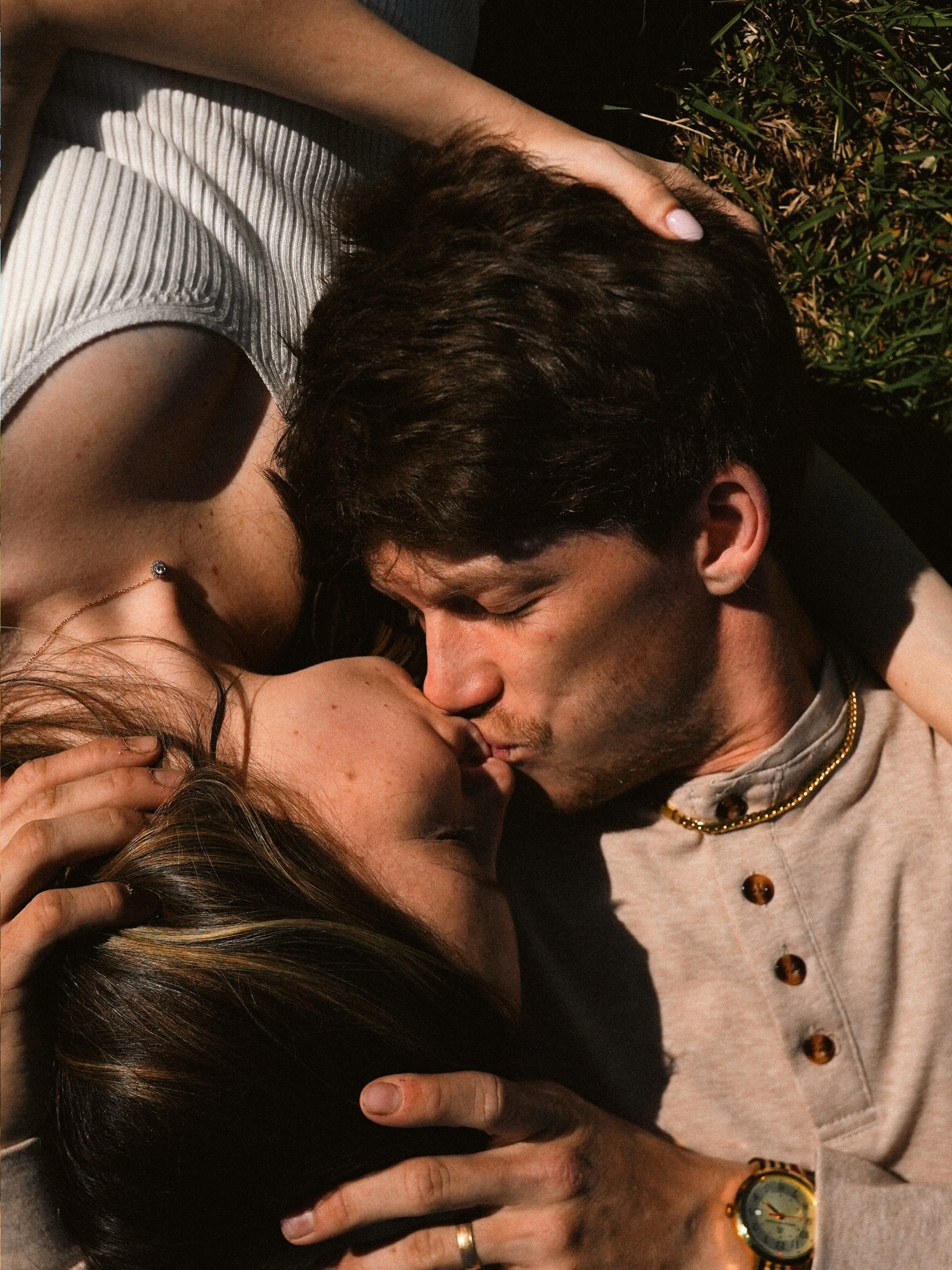 A young couple is lying on the grass, touching foreheads and kissing.