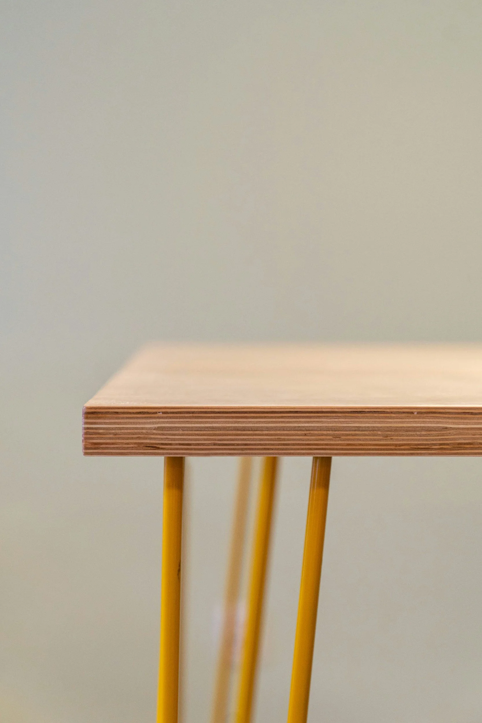 Close-up of a wooden table with yellow legs against a neutral wall.