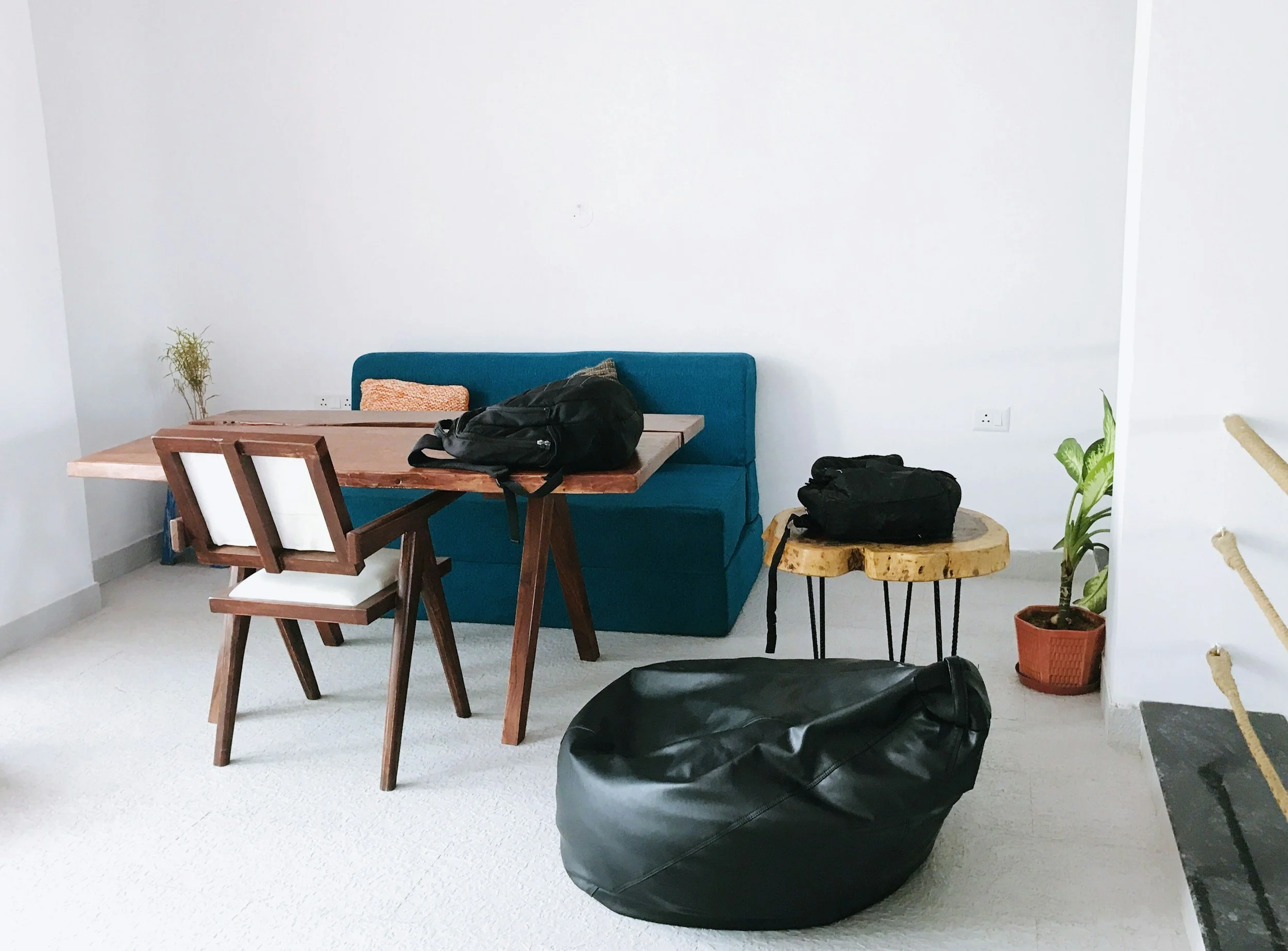 Living room with wooden dining table, teal bench, four chairs, potted plants, black bag, and white walls.