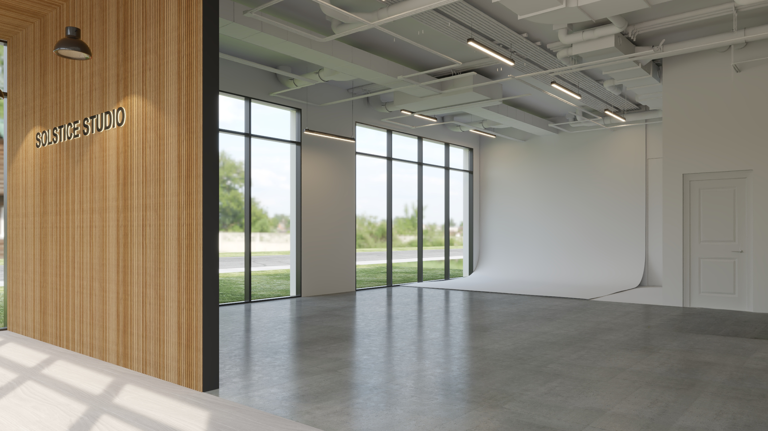 Interior of a modern building with large floor-to-ceiling windows, wood-paneled wall with illuminated sign that reads 'SOLSTICE STUDIO', exposed ceiling with ducts and lighting, and a curved white backdrop.