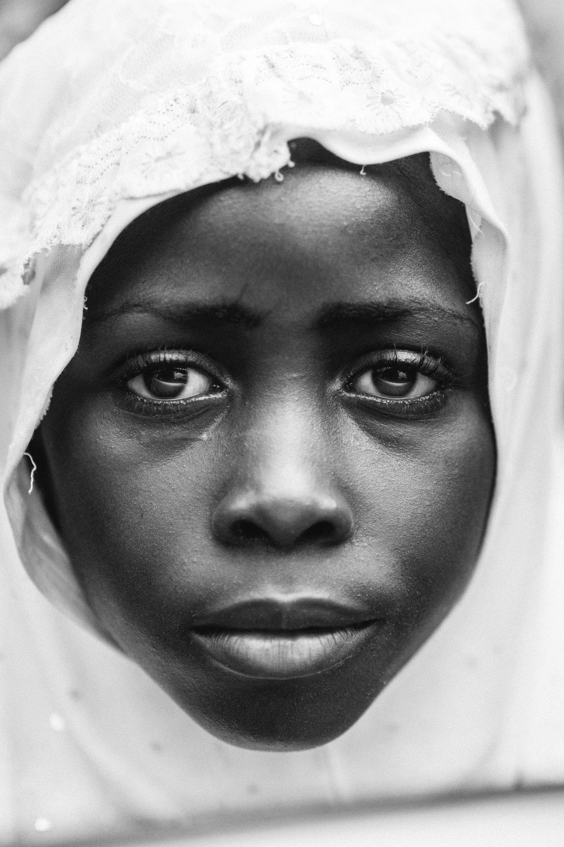 Photo of the black hijabi muslim girl. A close shot portrait with reflections on her eyes. She has white scarf on her head and looks very wise.